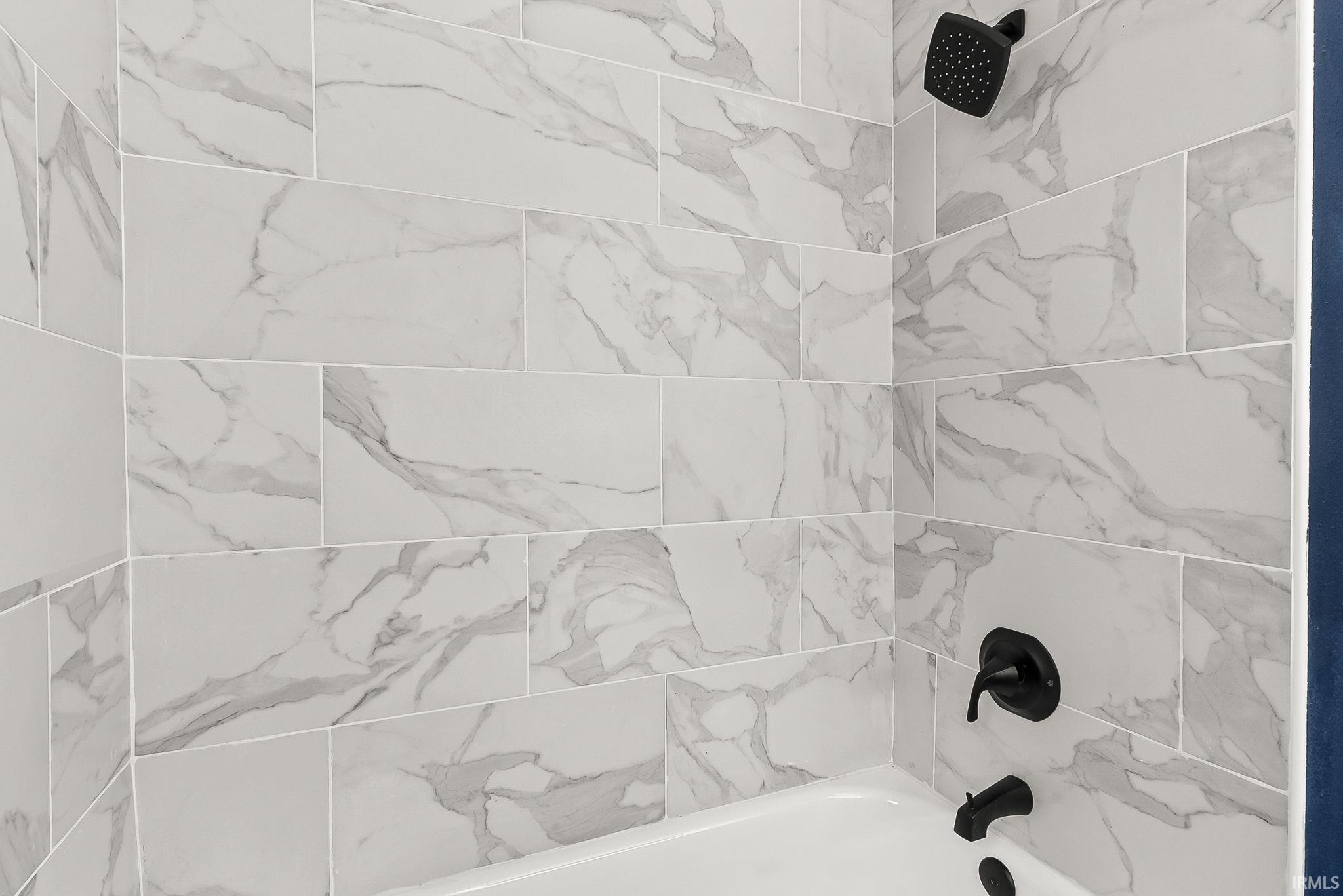 Tub-shower combination featuring white subway tile with gray veining, black shower head, and black faucet fixtures