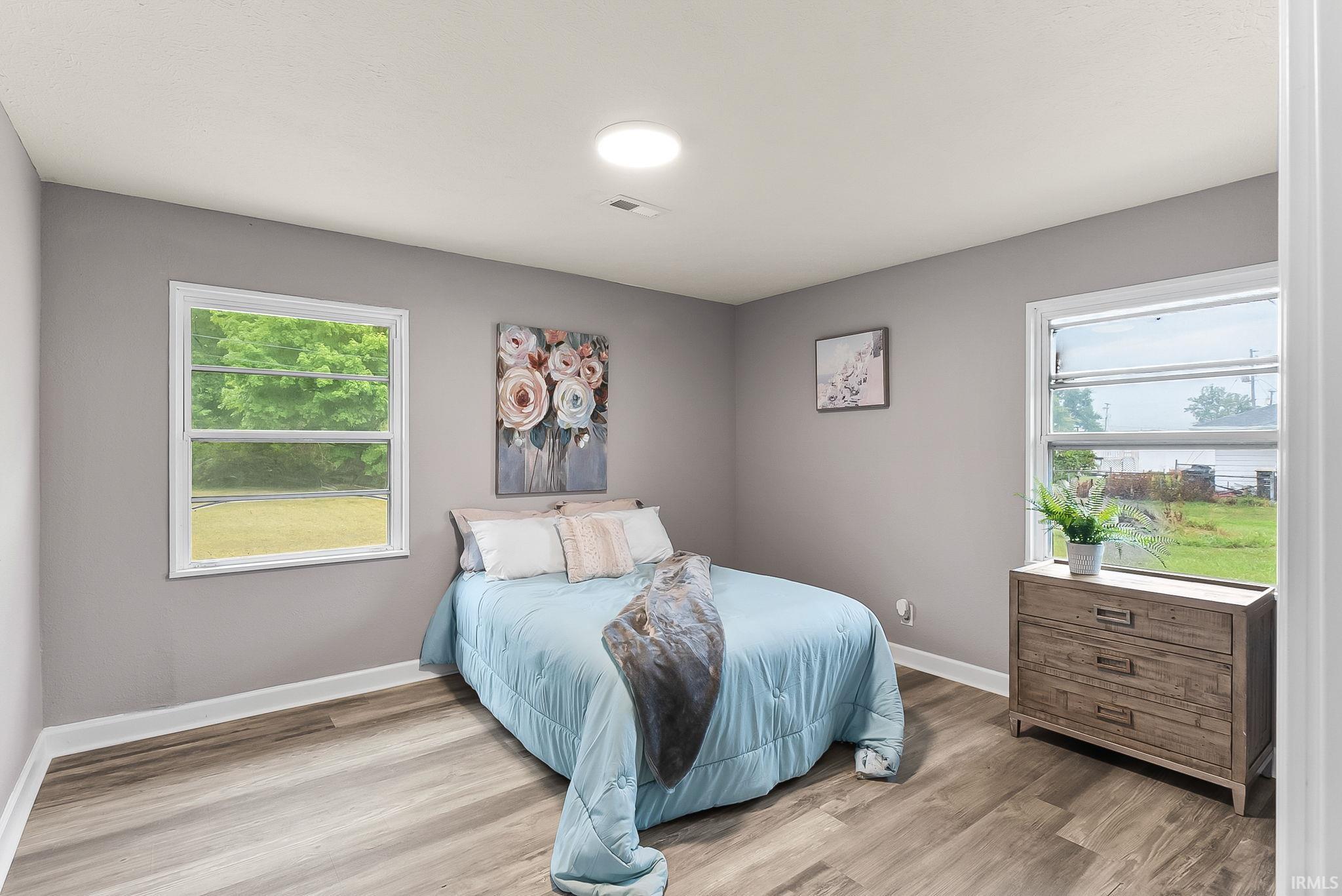 Room featuring wood-finish flooring, light grey walls, white baseboards, and two white-framed windows