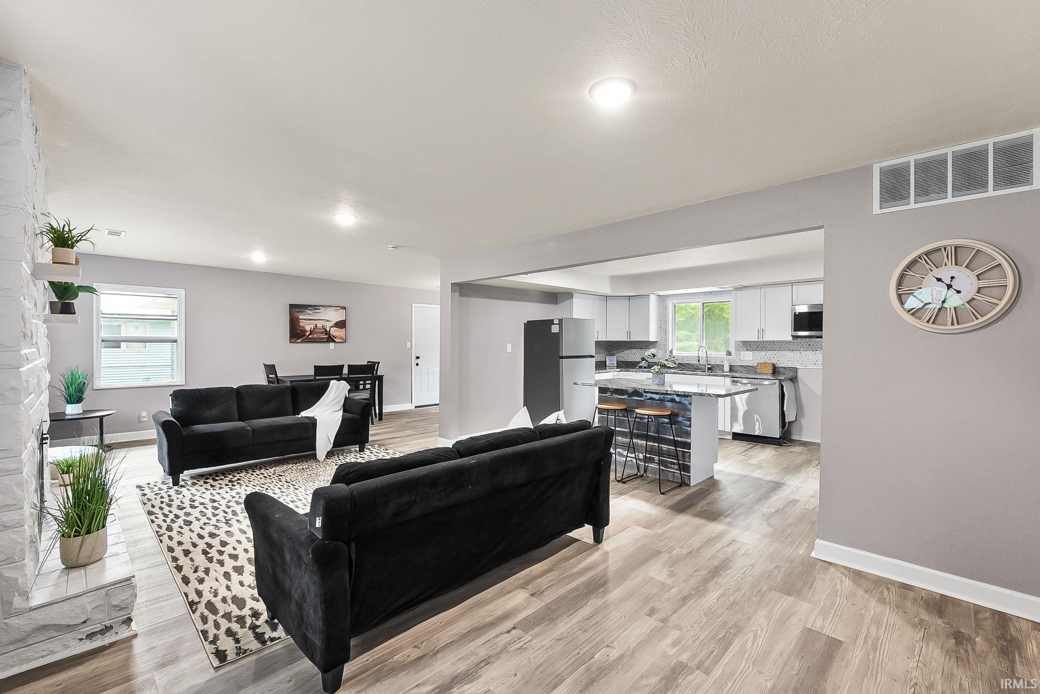 Open-concept living area with wood-finish flooring, a white brick fireplace, and recessed lighting