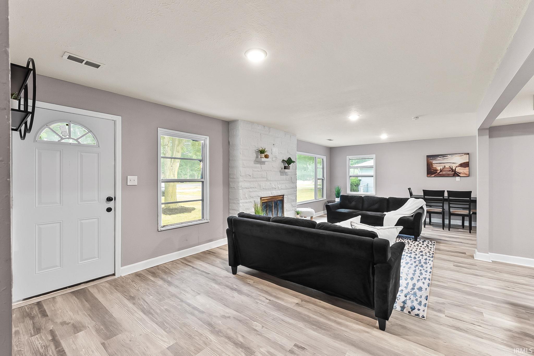 Open-concept living area featuring wood-finish flooring, recessed lighting, and a white brick fireplace