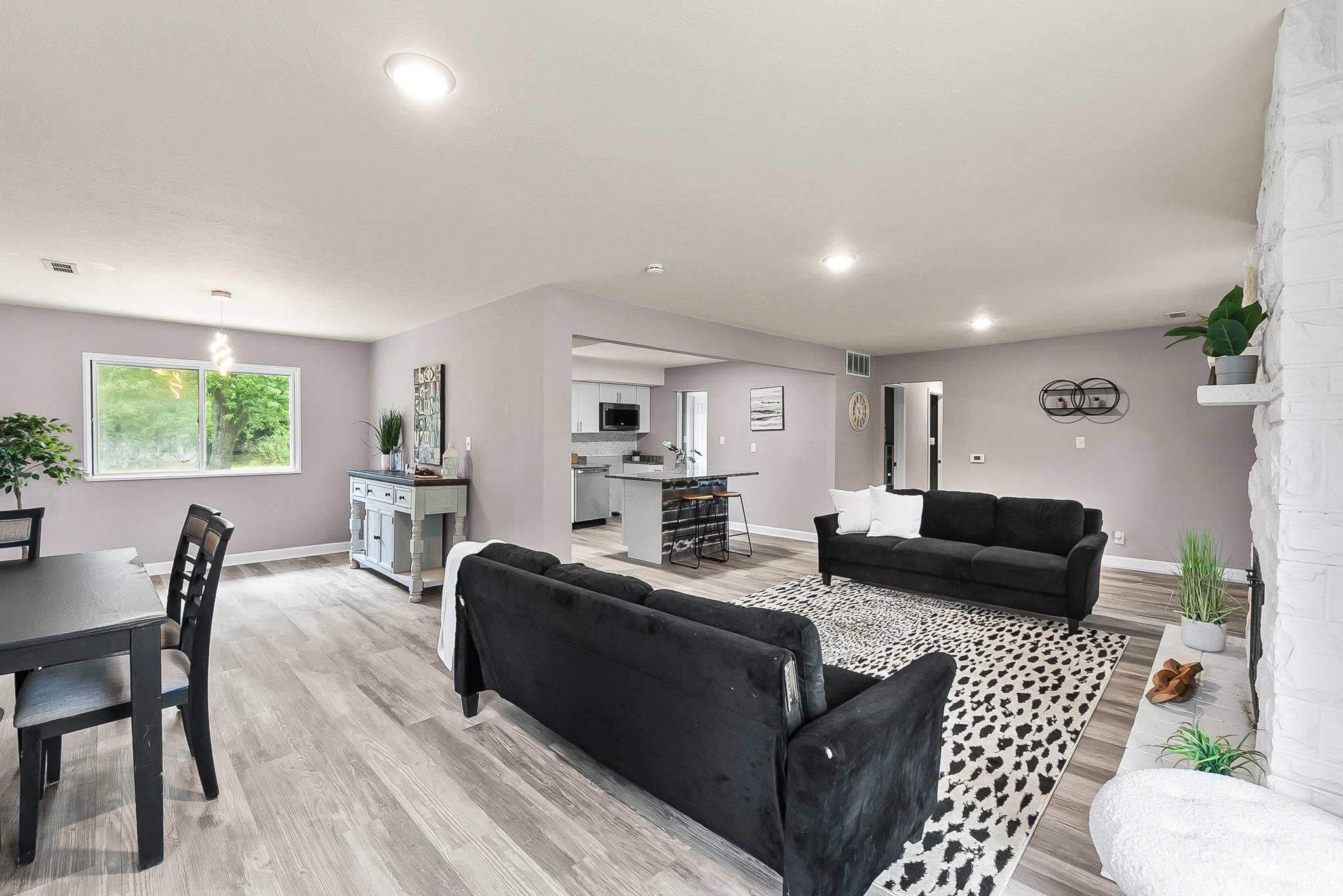 Open-concept living space featuring wood-finish flooring, recessed lighting, and a white brick fireplace