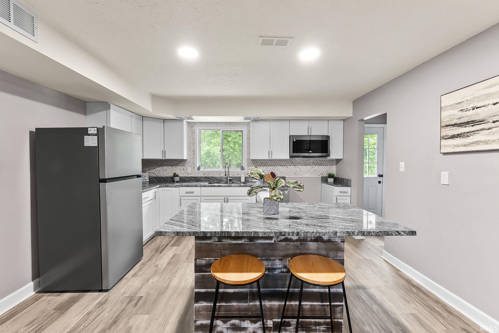 Modern kitchen featuring a central island with a granite countertop, light gray cabinetry, and wood-finish flooring