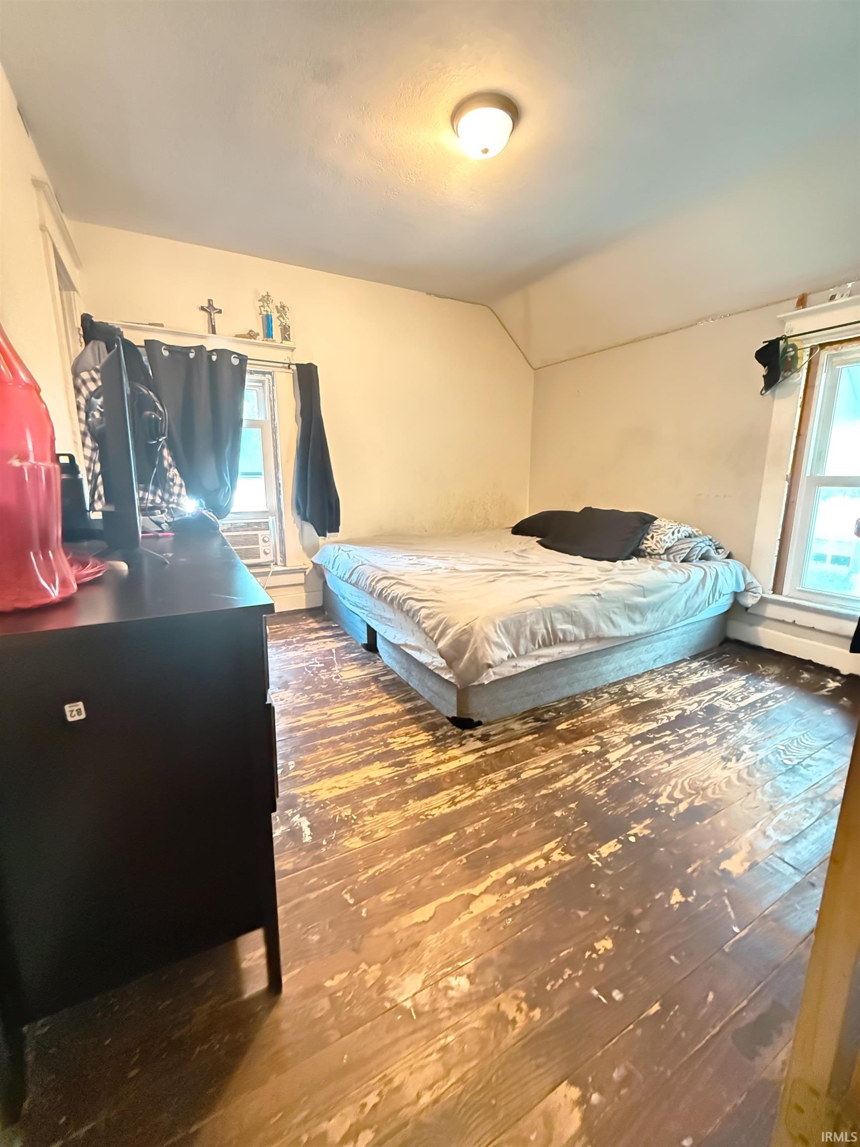 Bedroom featuring natural wood flooring, two windows providing natural light, a ceiling-mounted light fixture, and textured walls