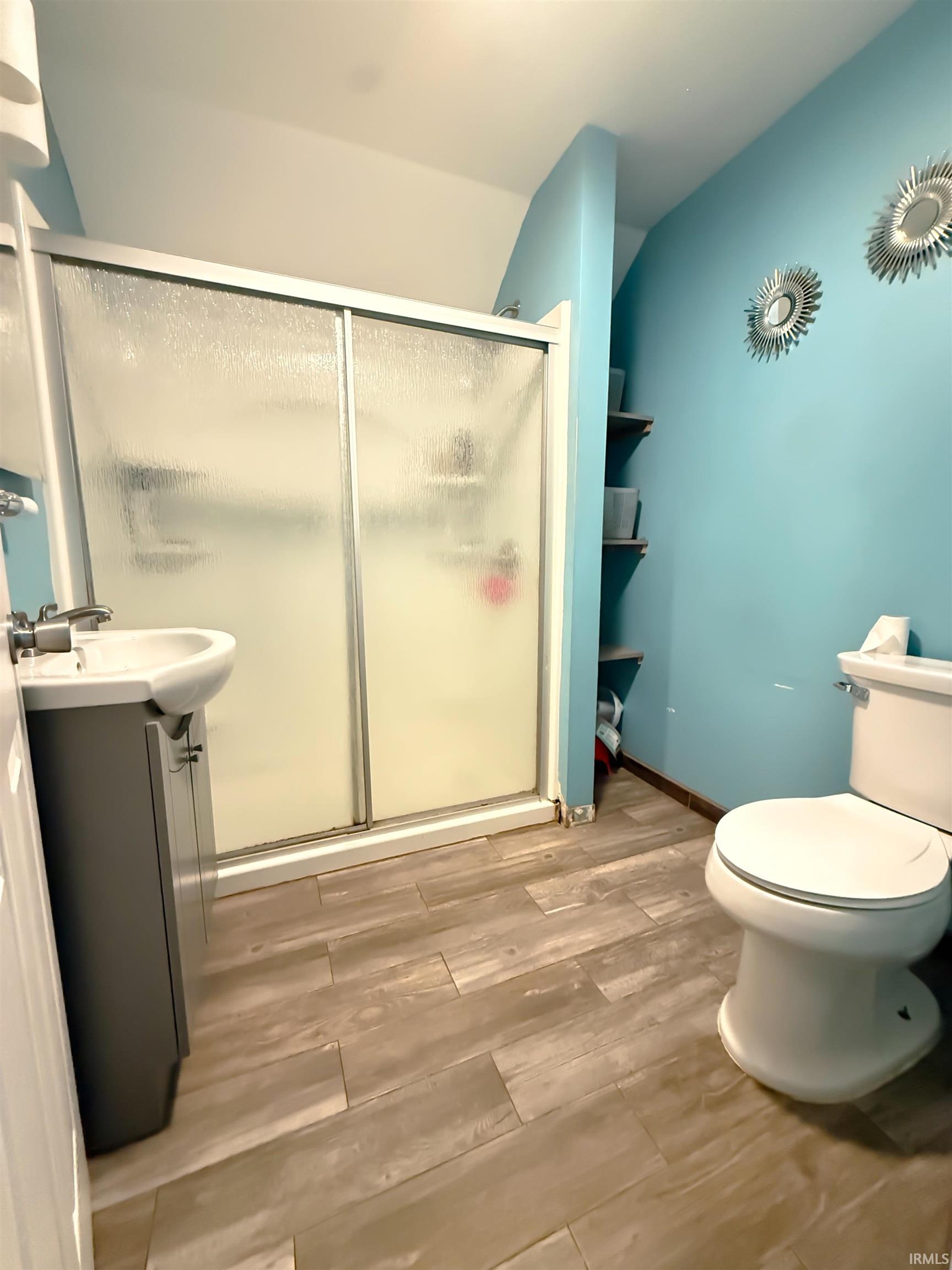 Bathroom featuring a shower with frosted sliding glass doors, a vanity with an integrated sink, built-in shelving, and wood-finish flooring