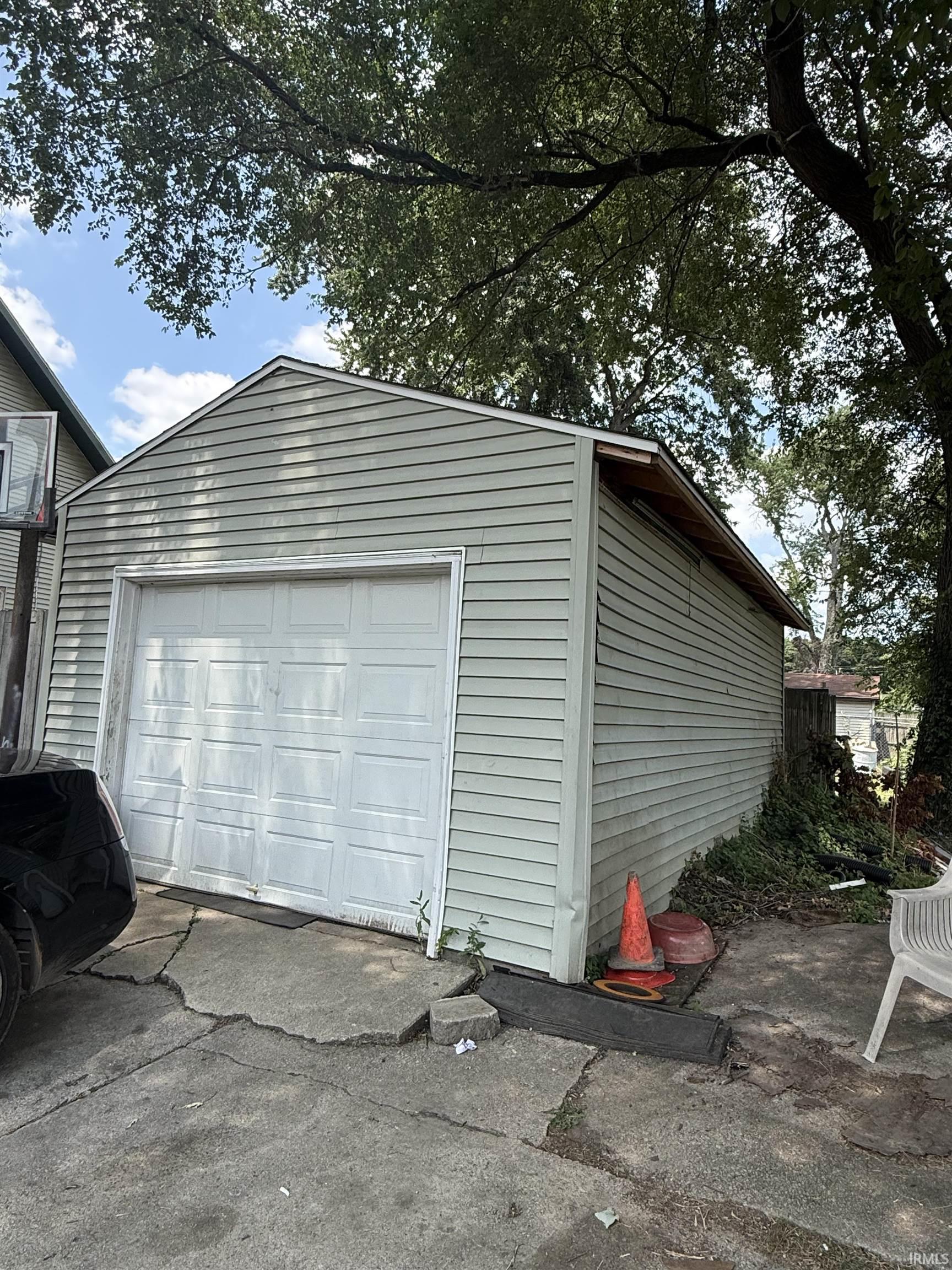 Detached garage featuring light-colored siding, a white overhead door, and a gable roofline