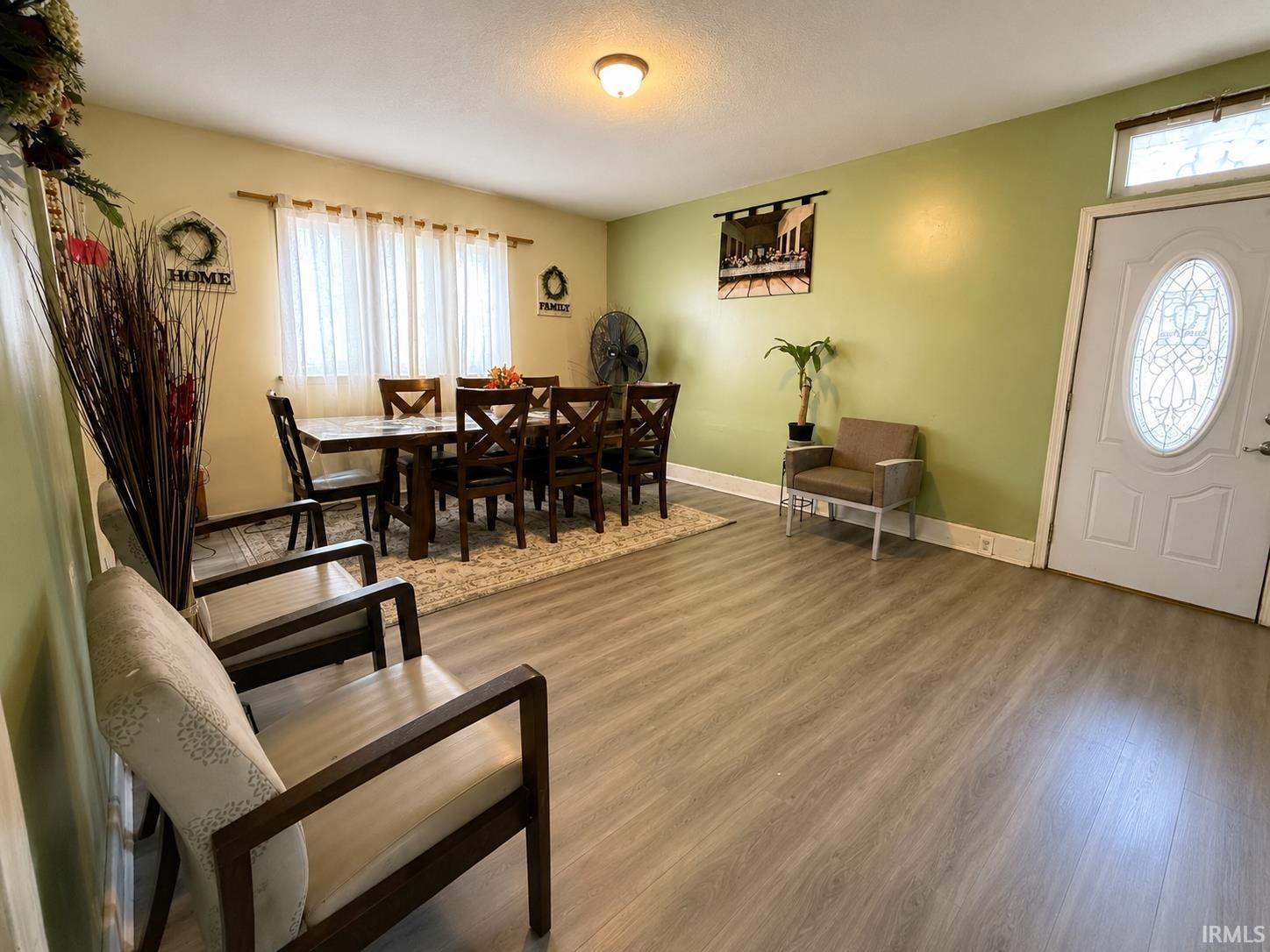 Open living area featuring wood-finish flooring, a decorative front door with an oval-shaped glass insert, and a transom window