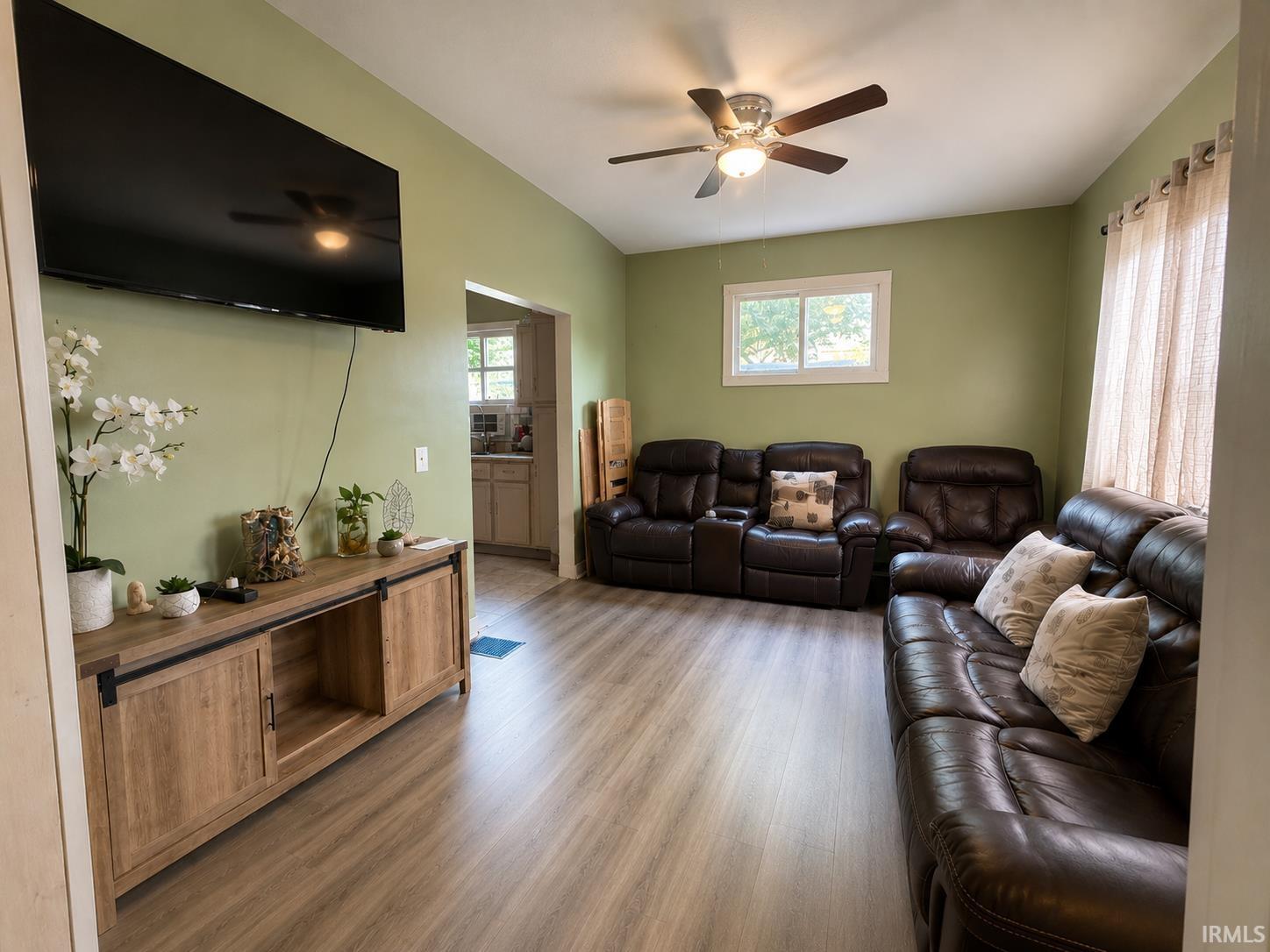 Spacious living area featuring wood-finish flooring, a ceiling fan with integrated lighting, and ample natural light from a prominent window