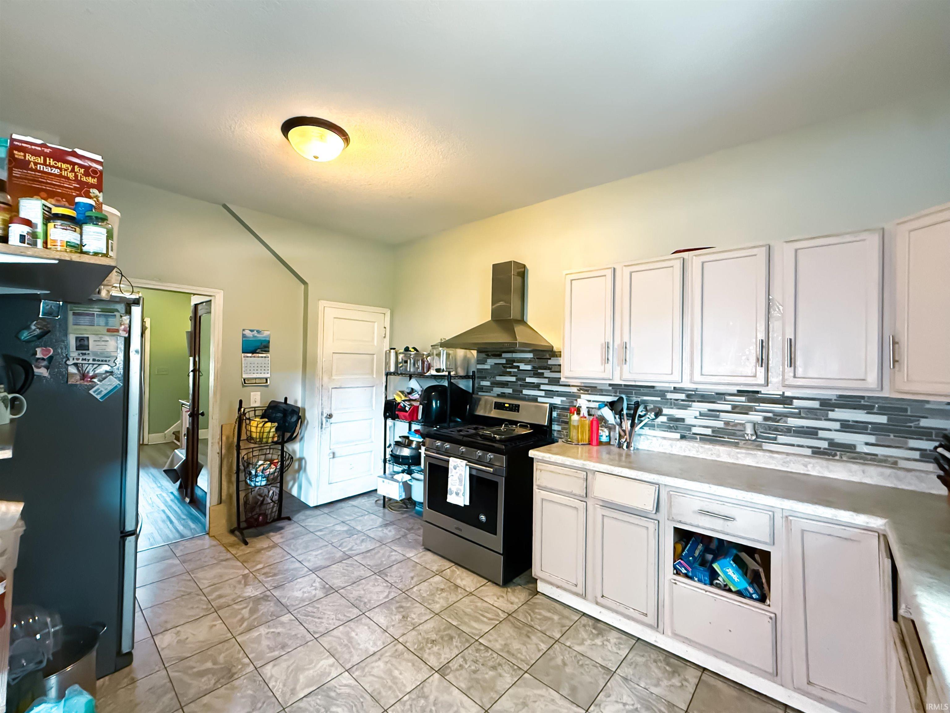 Kitchen featuring light-toned cabinetry, a modern range hood, and a tile backsplash with varied gray and white hues