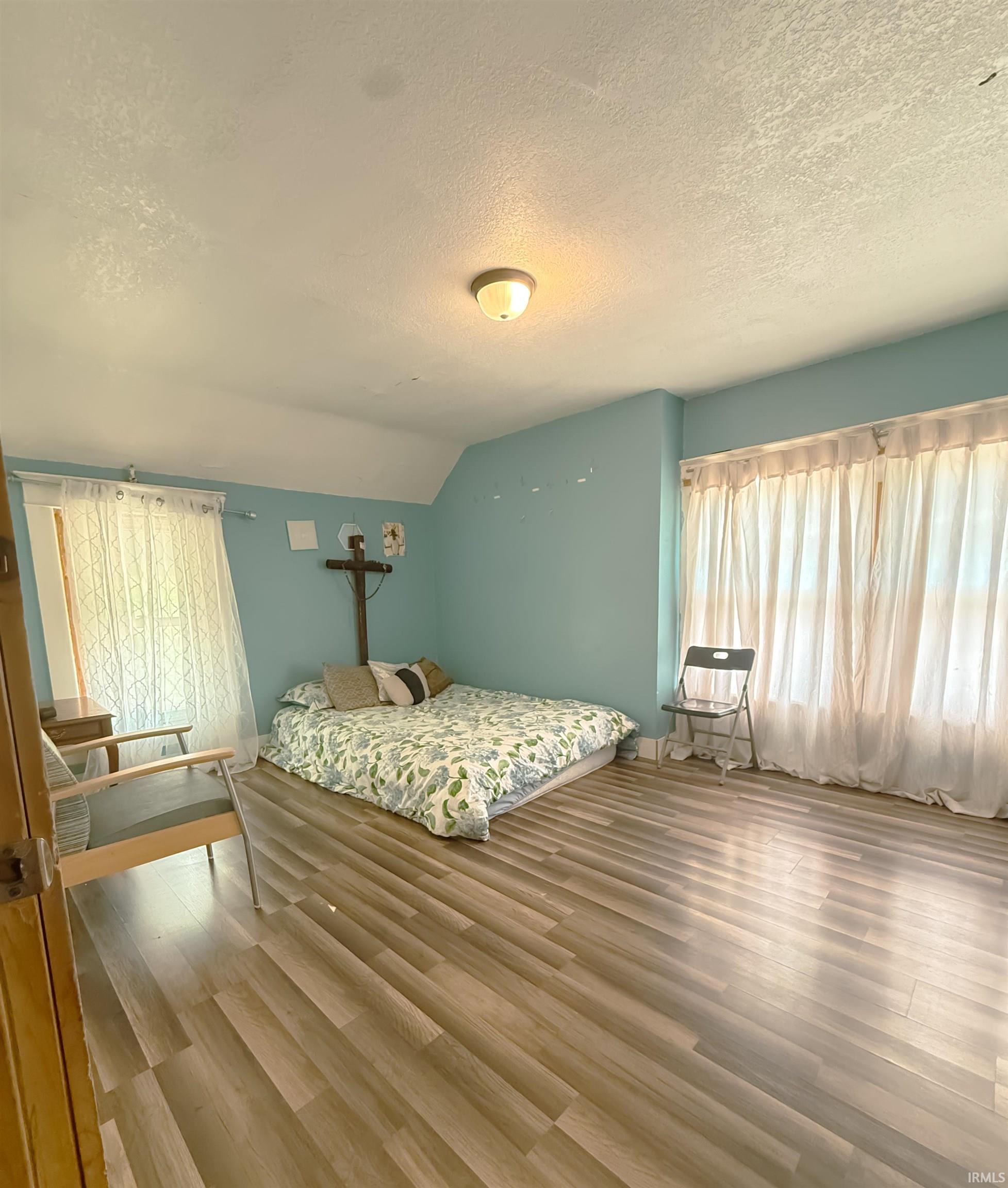 Spacious room featuring wood-finish flooring, light blue wall paint, and two large window openings providing ample illumination
