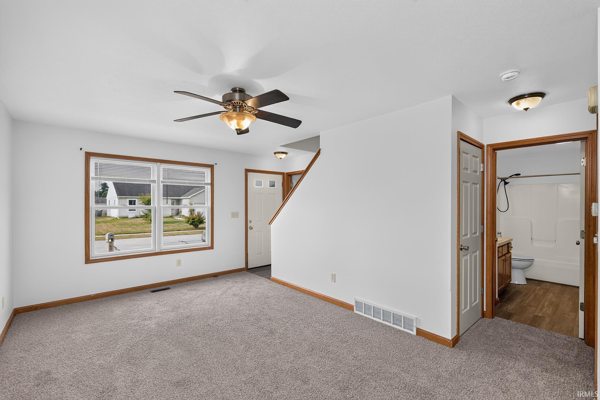 Living area featuring light gray carpeting, white walls, and a multi-pane window with wood-finish trim