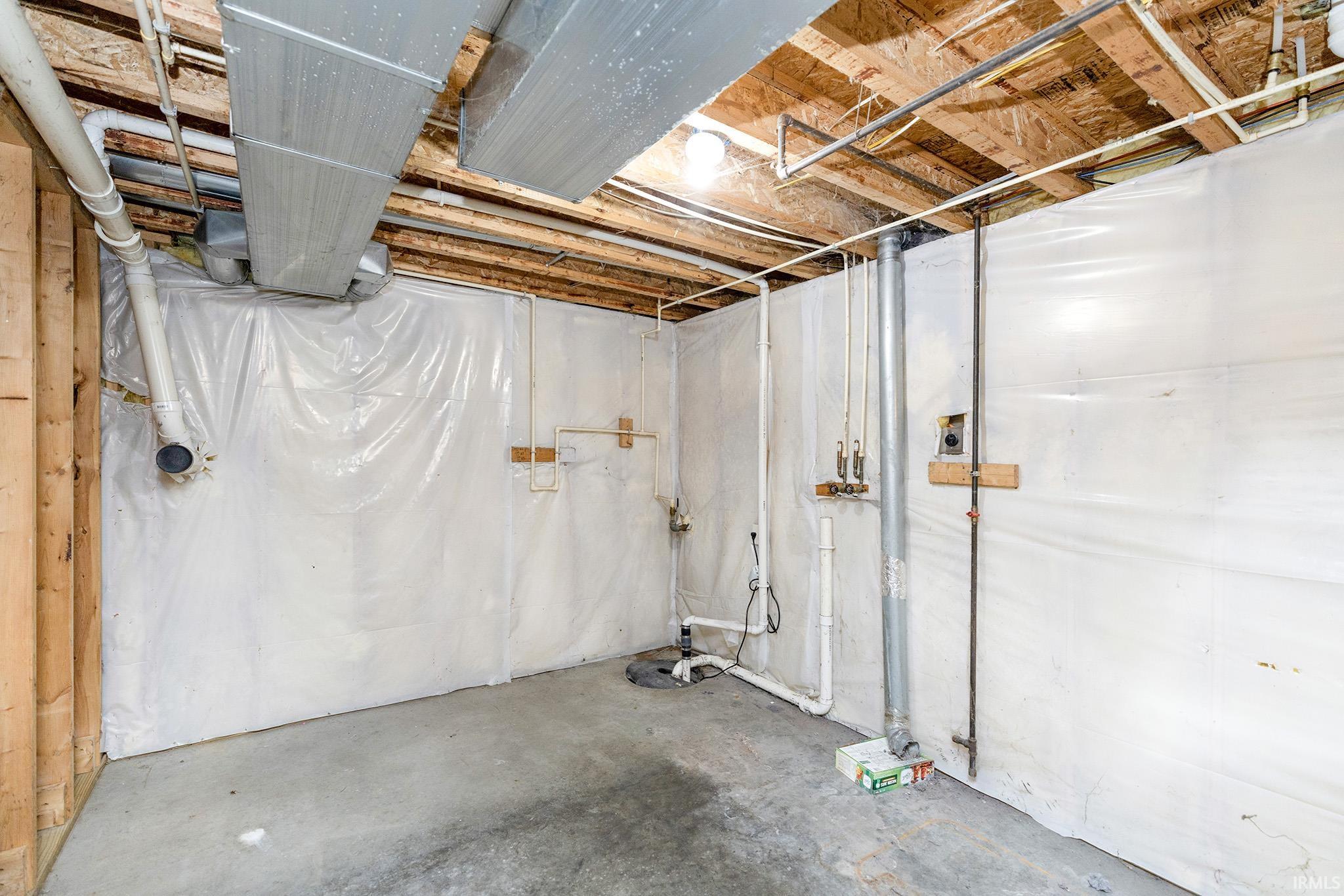 Unfinished basement space featuring exposed wooden joists, concrete flooring, and perimeter wall insulation