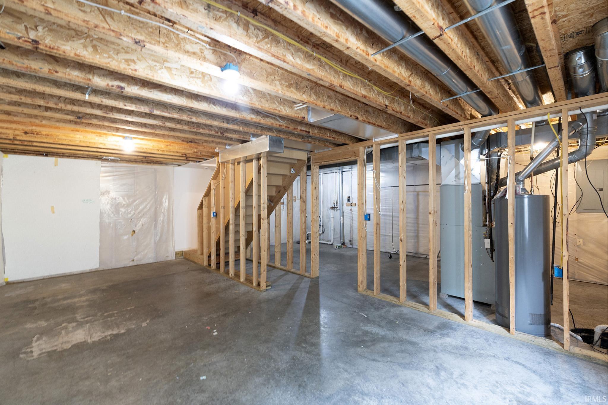 Unfinished basement featuring exposed wood joists, concrete flooring, and partial framing for future development