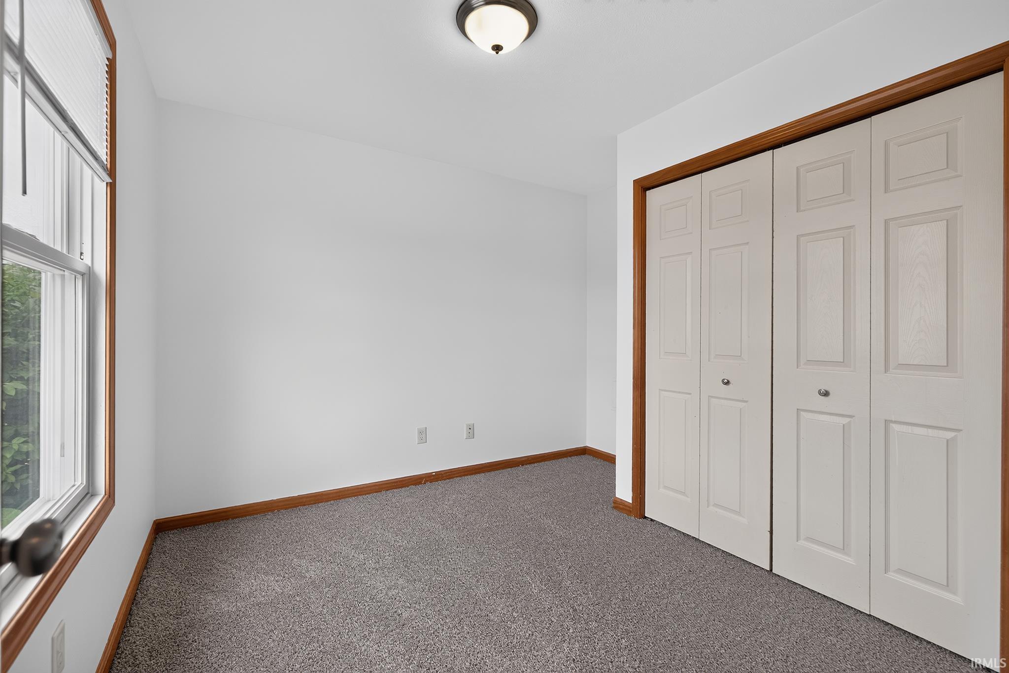 Room featuring neutral wall tones, gray carpeting, a built-in closet with bi-fold doors, and a double-hung window with a wood-finish frame