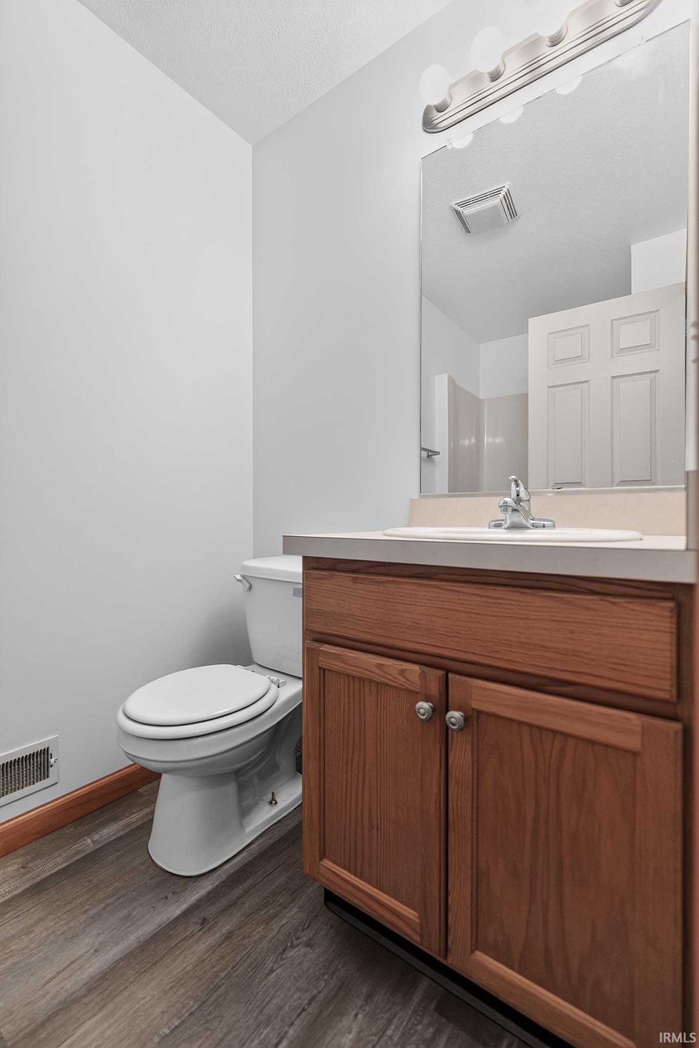 Bathroom featuring a wood-finish vanity with countertop sink, wall-mounted mirror, and overhead lighting fixture