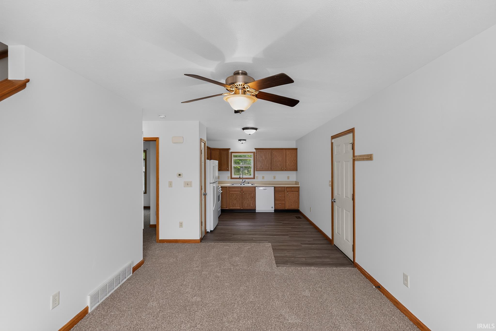 Open-concept living area with neutral carpeting and a ceiling fan with integrated lighting
