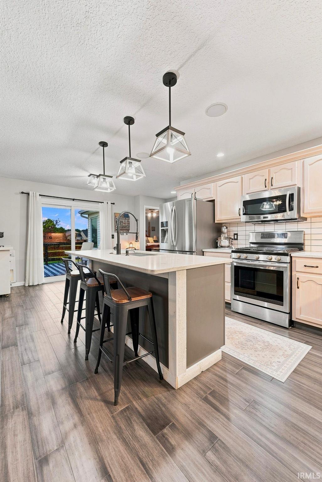 Kitchen featuring a central island with countertop seating, wood-finish flooring, stainless steel appliances, and pendant lighting