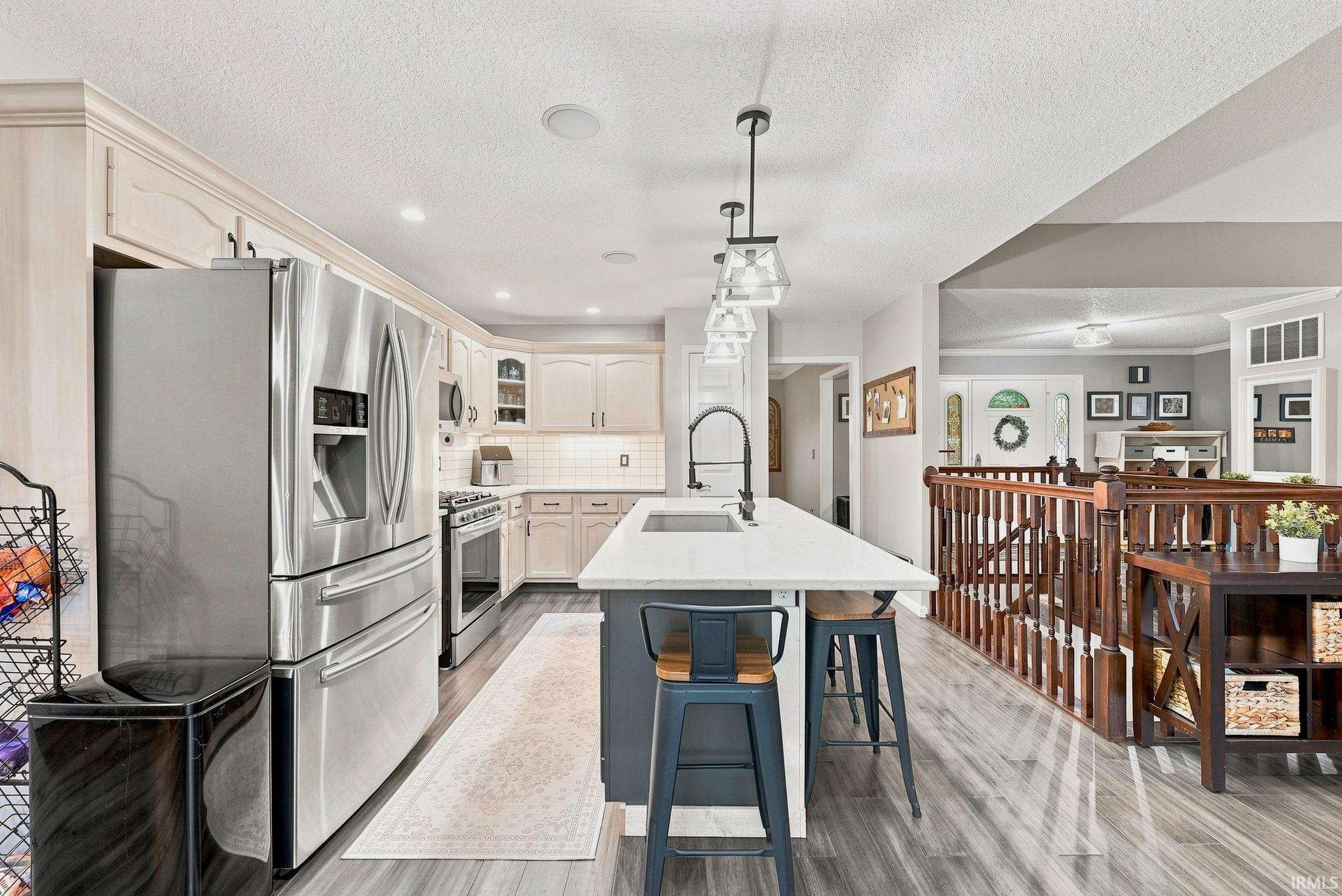 Modern kitchen with stainless steel appliances, light-toned cabinetry, and a central island featuring a sink and pendant lighting