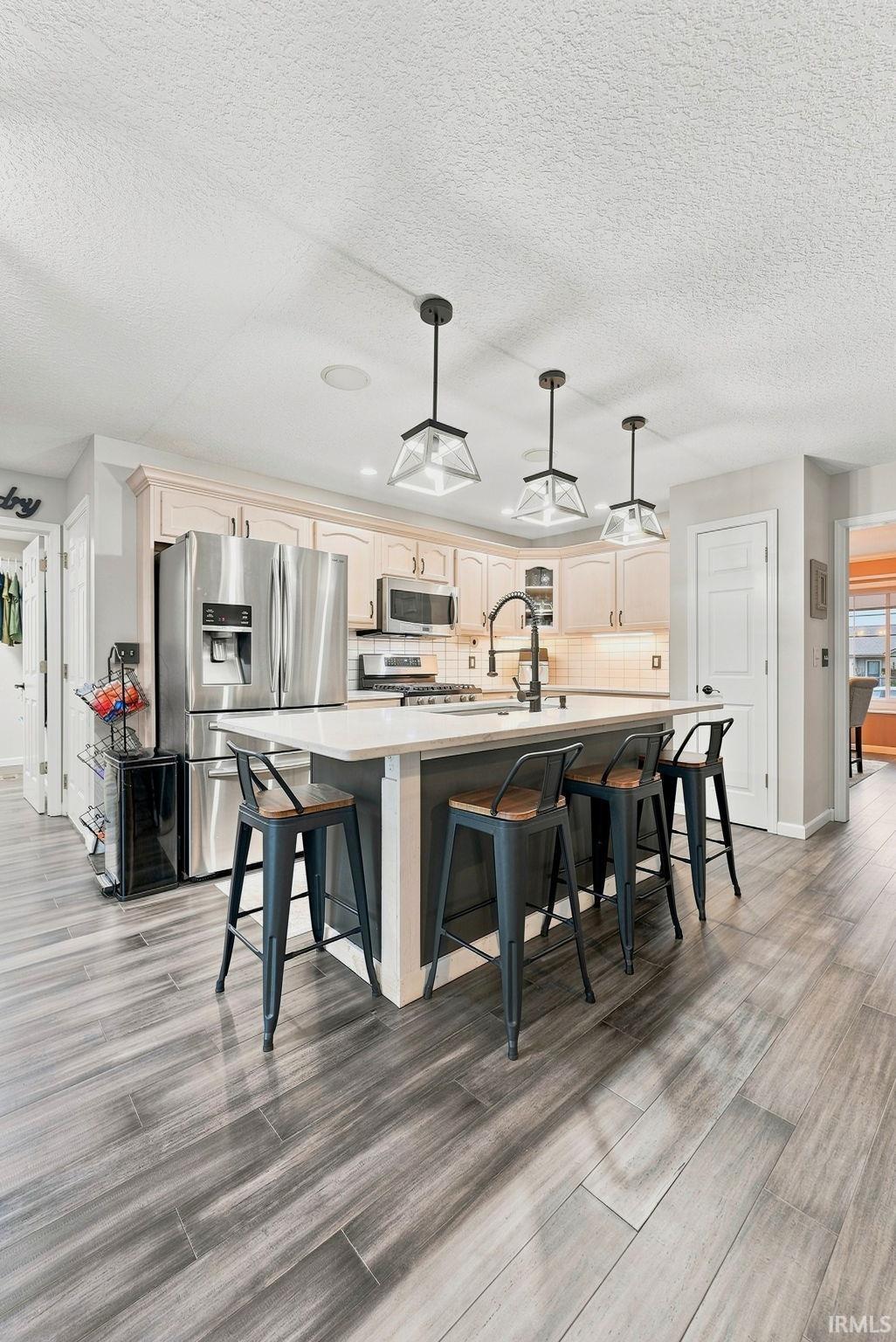 Contemporary kitchen featuring a spacious island with seating, stainless steel appliances, light-toned cabinetry, a dark faucet, and plank-style flooring