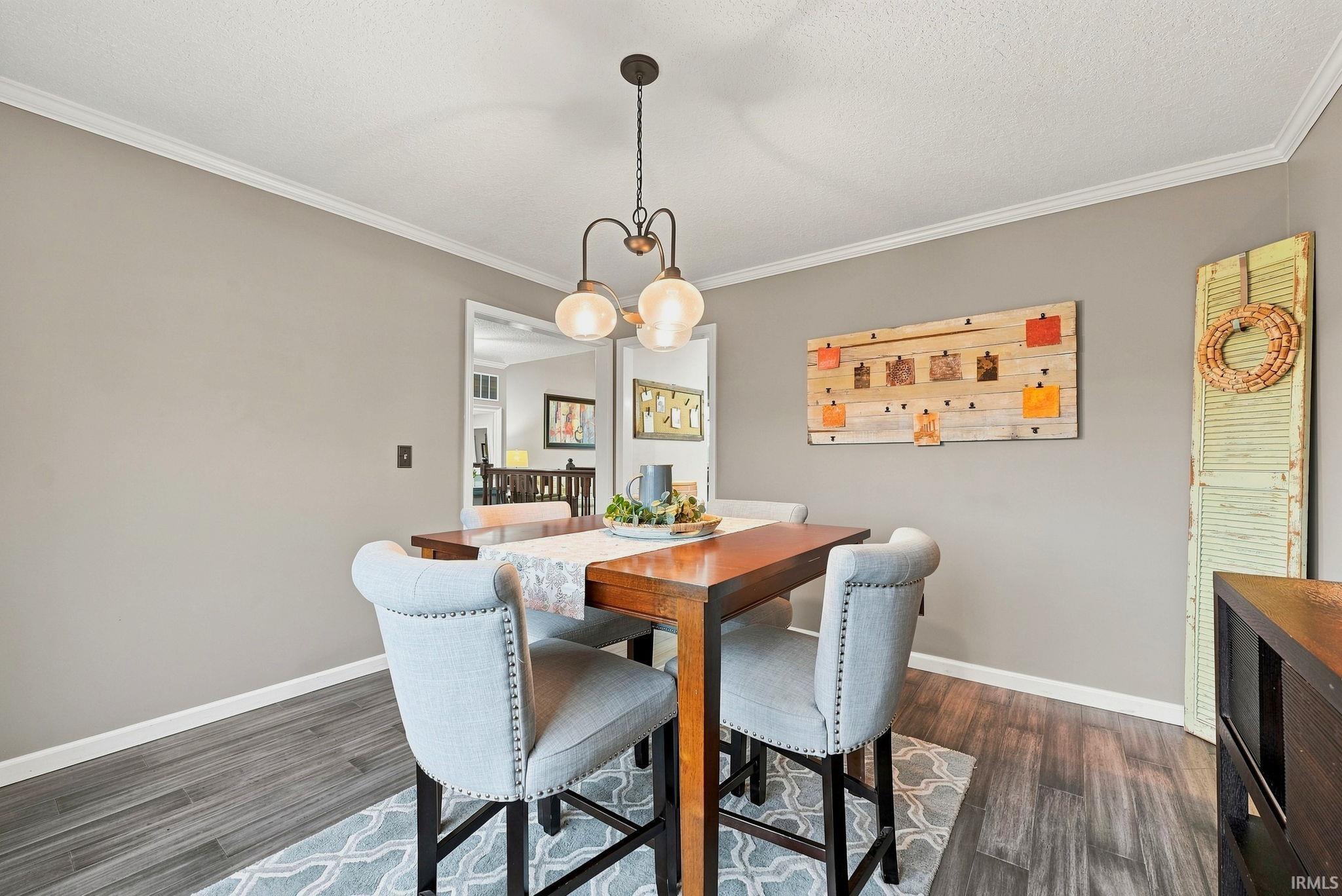 Dining area featuring a contemporary chandelier, wood-finish flooring, neutral wall paint, white crown molding, and white baseboards