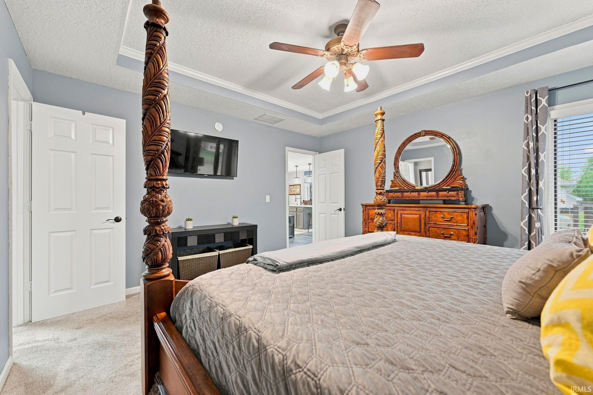 Spacious bedroom featuring light blue walls, tray ceiling, and ceiling fan with integrated lighting