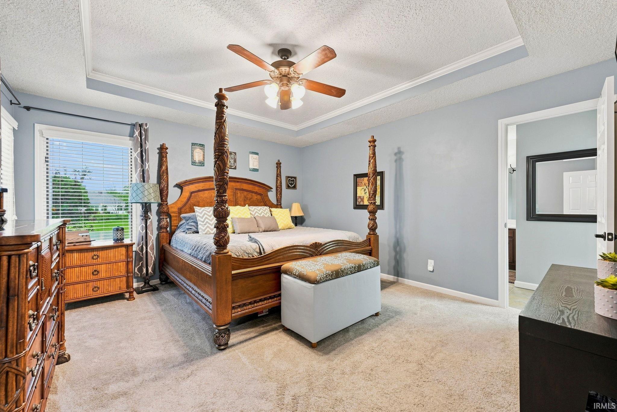 Recessed tray ceiling with crown molding, ceiling fan, and carpeted flooring