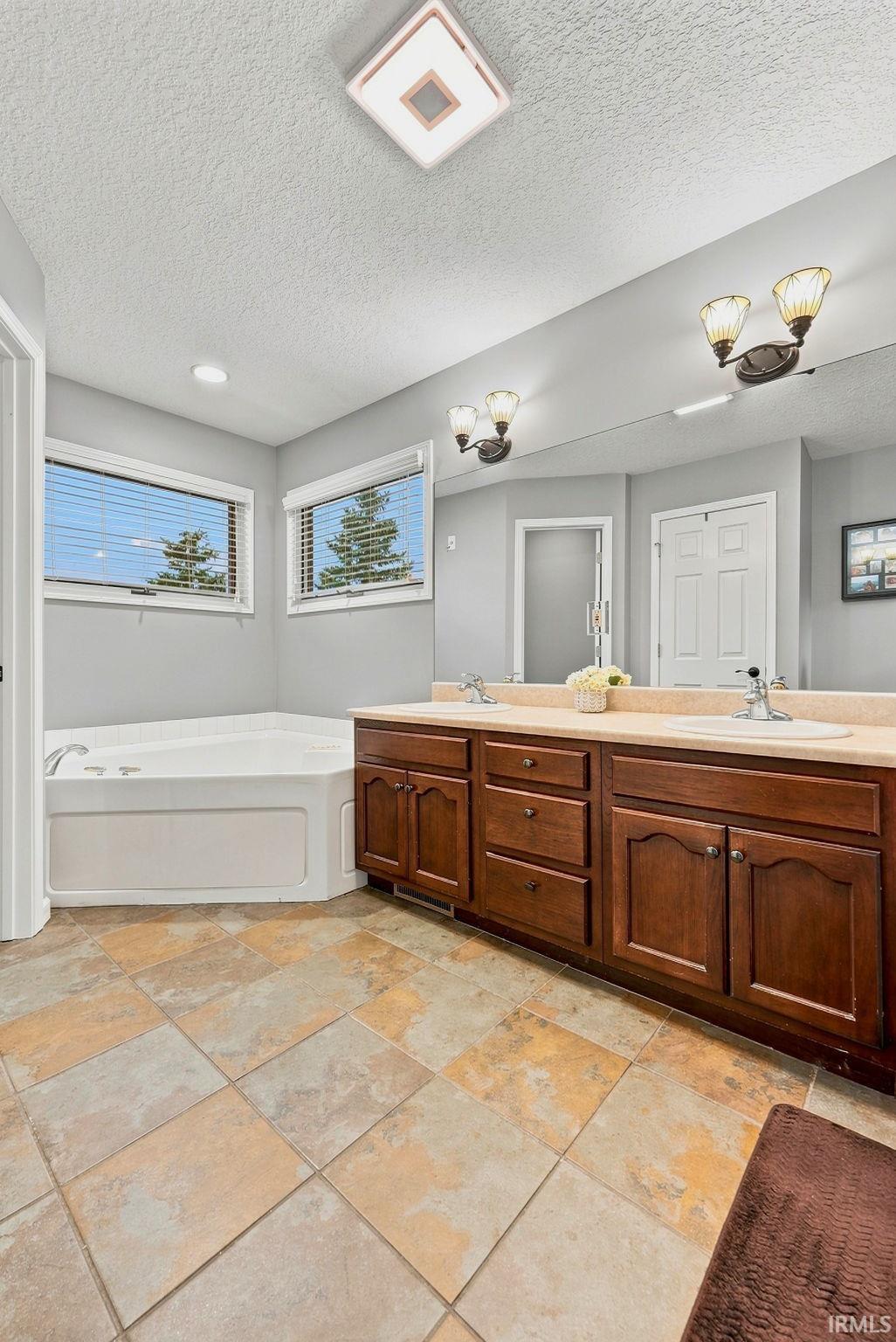 Bathroom featuring a dual vanity with wood cabinetry, light-toned countertop, and two sets of wall-mounted light fixtures