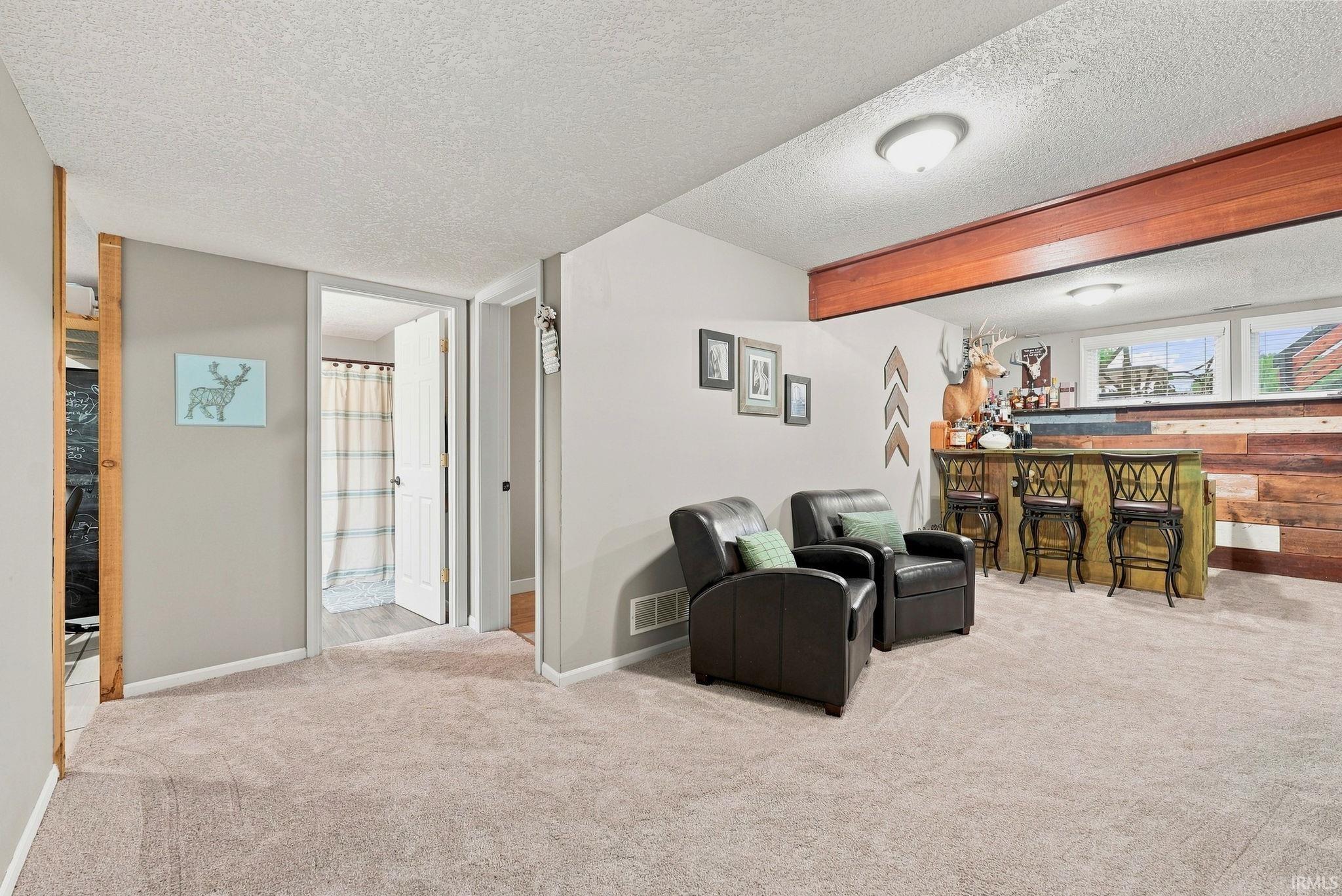 Finished basement space featuring a built-in bar with wood paneling, recessed lighting, and a neutral carpeted floor