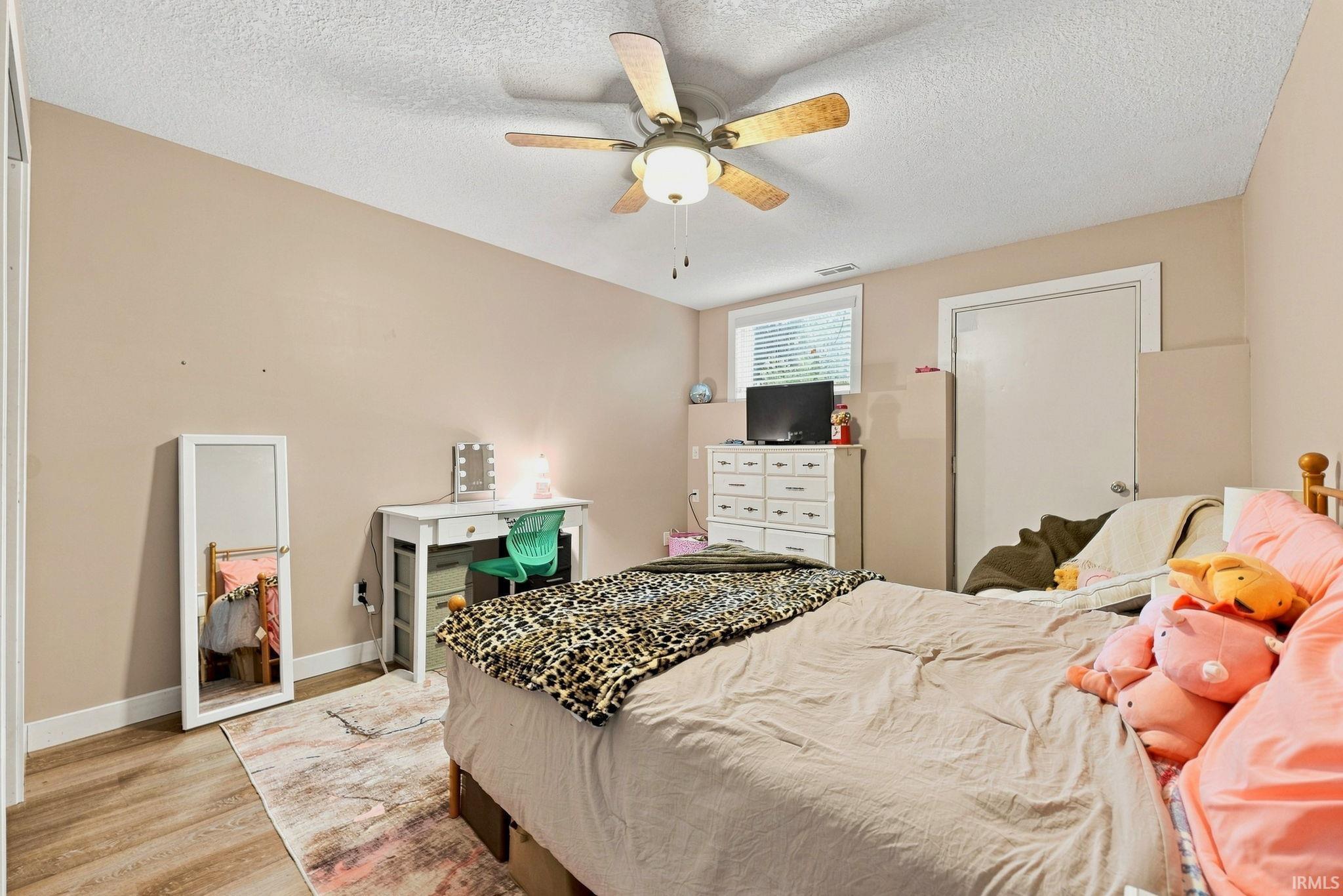Interior room featuring wood-finish flooring, a ceiling fan, and a window with blinds