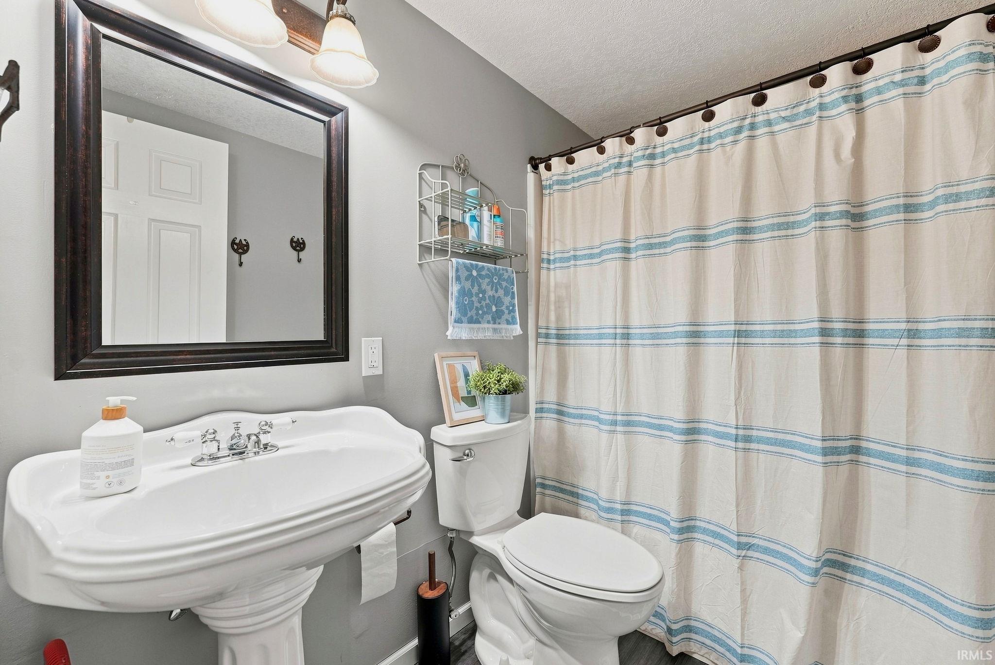 Bathroom featuring a pedestal sink with chrome fixtures, a framed wall mirror, and a wall-mounted light fixture