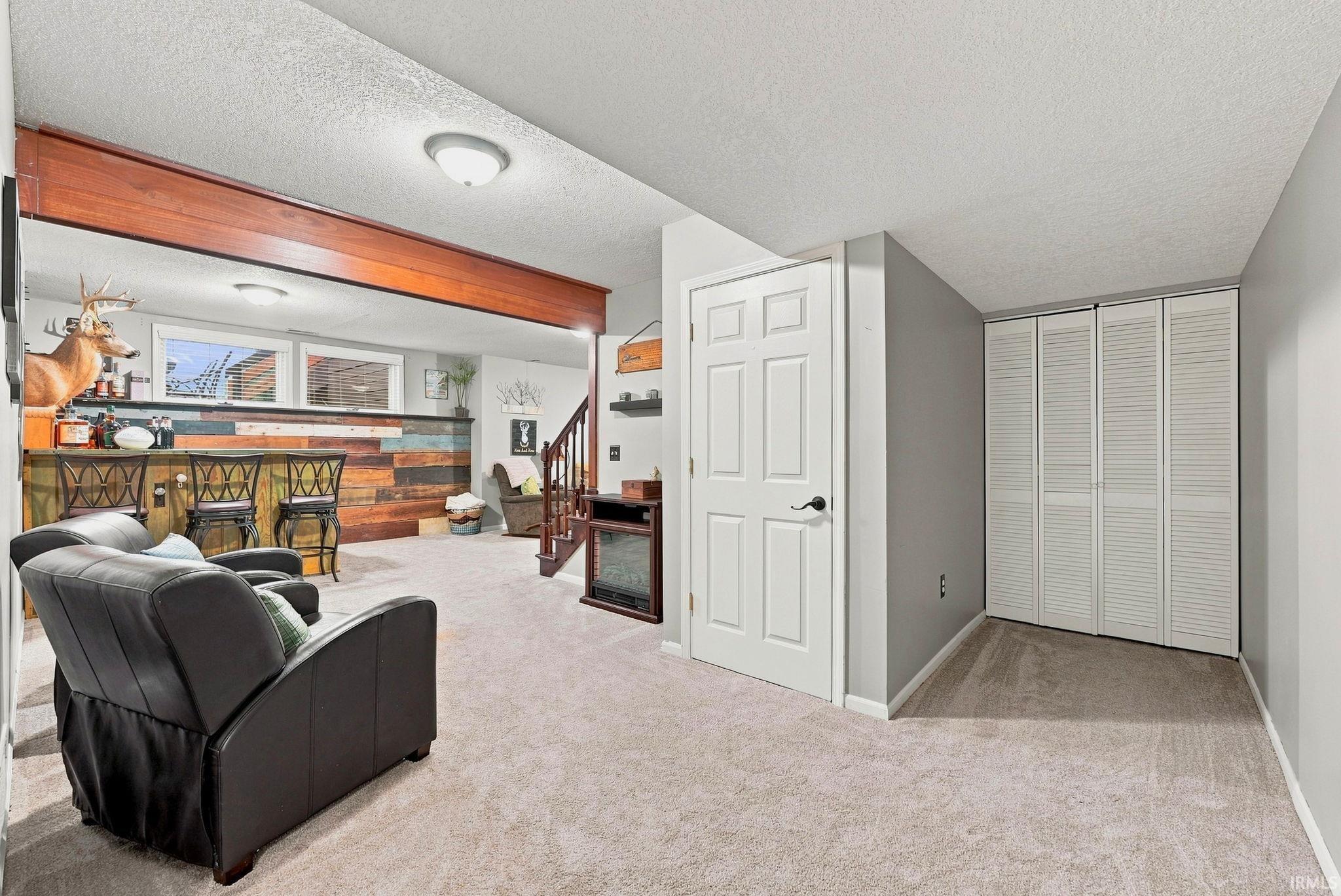Expansive carpeted area featuring a built-in wet bar with a wood-finish facade, a staircase with wood railings, and bi-fold closet doors