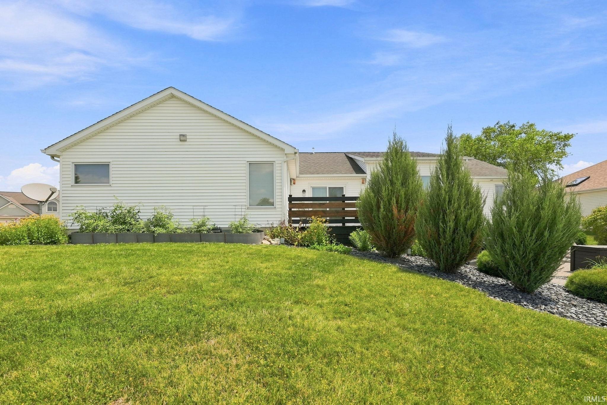 Expansive green lawn with mature evergreen trees and a raised garden bed