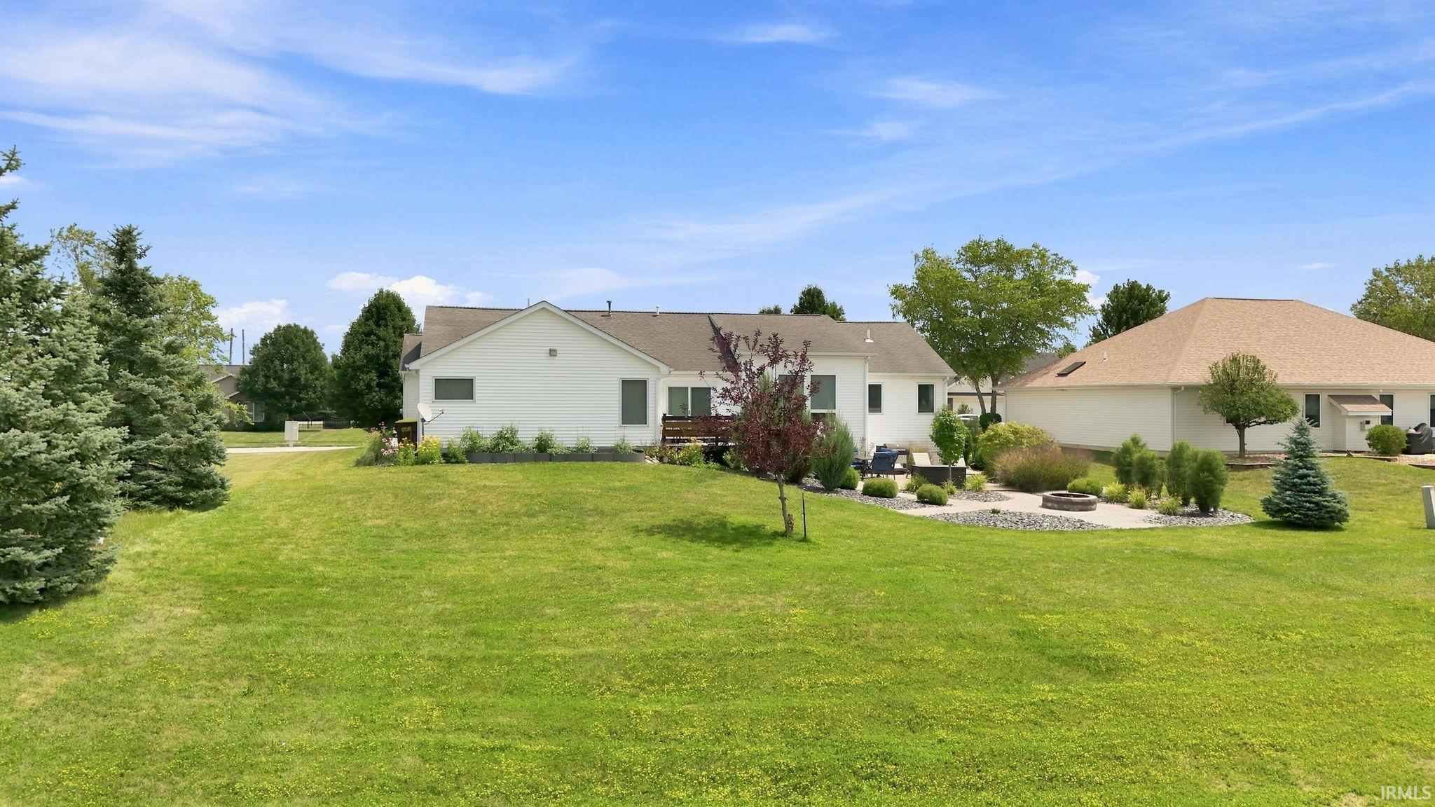 Expansive green lawn featuring a stone patio with a built-in fire pit, surrounded by mature landscaping and shrubbery