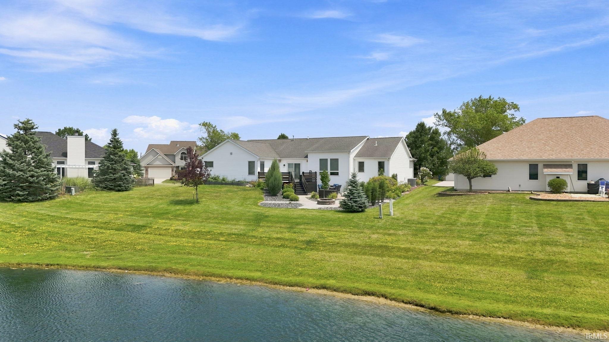 Rear exterior featuring an elevated deck, paver patio, and mature landscaping overlooking a pond