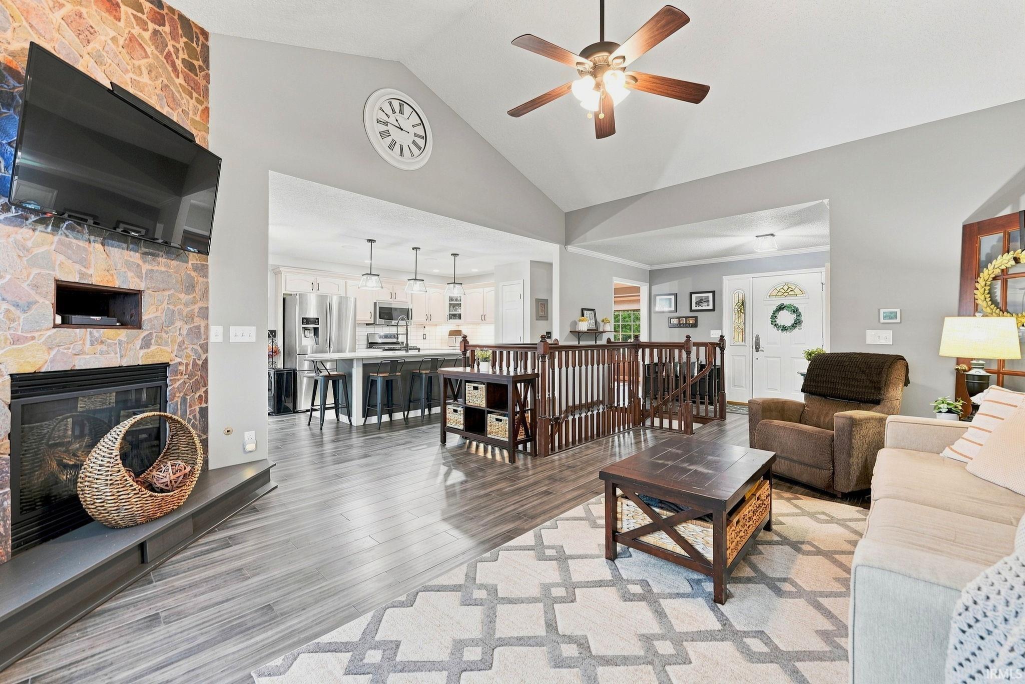 Spacious living area featuring a stone-clad fireplace with mantel, vaulted ceiling with a fan, and wood-finish flooring