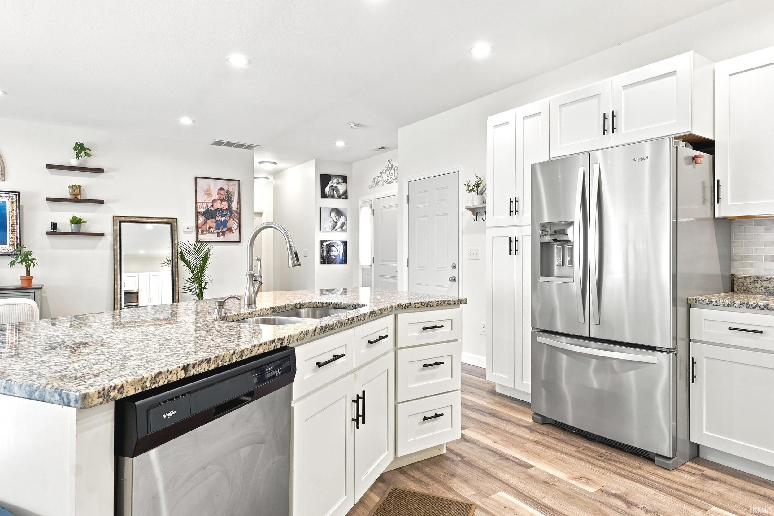 Kitchen featuring a granite-topped island with an undermount sink and gooseneck faucet, stainless steel dishwasher, white shaker-style cabinetry with matte black hardware, stainless steel French door refrigerator, and wood-finish flooring