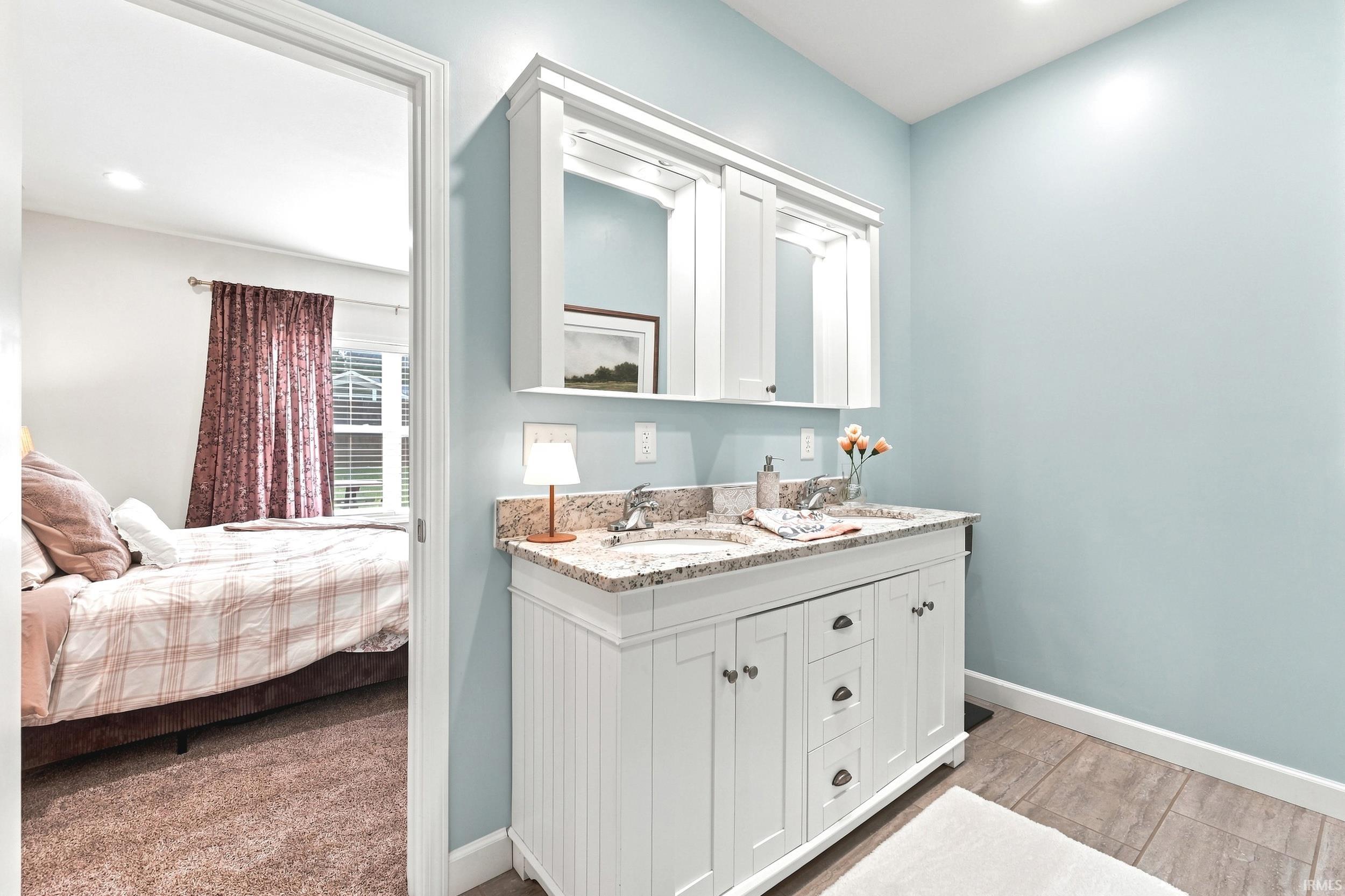 Bathroom vanity featuring dual sinks, a granite countertop, and white shaker-style cabinetry with dark hardware