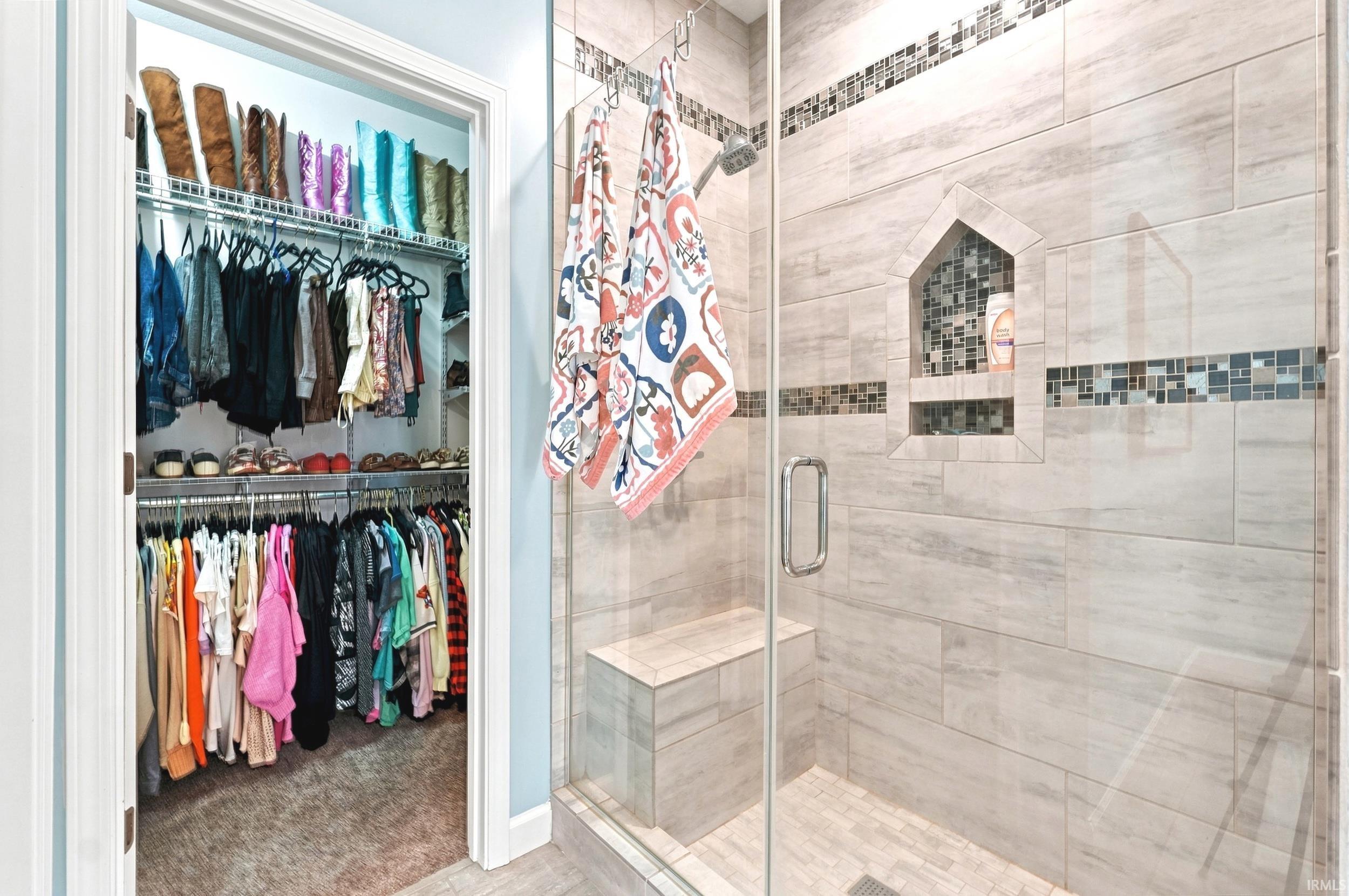 Glass-enclosed shower featuring large format tile, mosaic tile accents, a built-in bench, and an integrated niche