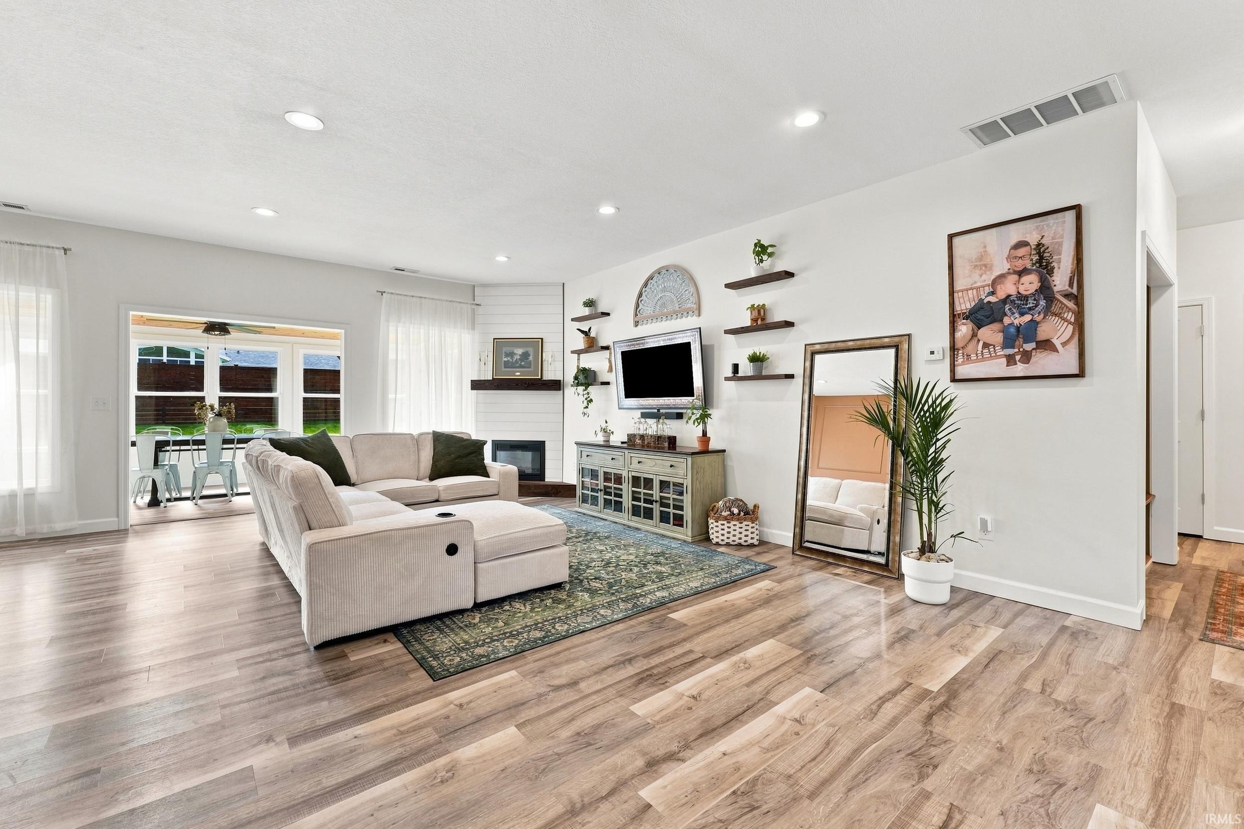 Open-concept living space featuring wood-finish flooring, recessed lighting, and a corner fireplace with a dark mantel