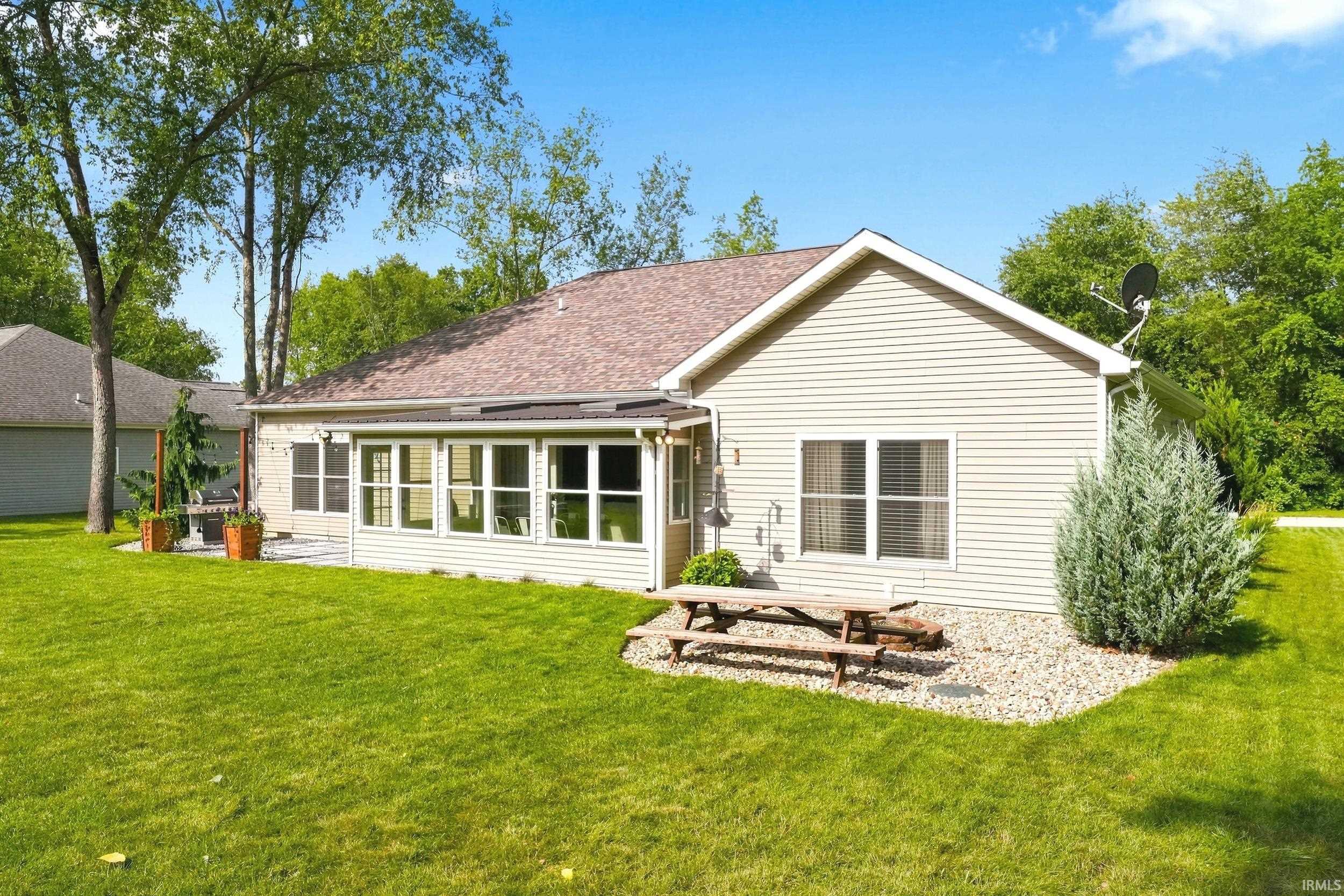 Expansive backyard featuring a manicured lawn, a sunroom with multiple windows, and a patio area