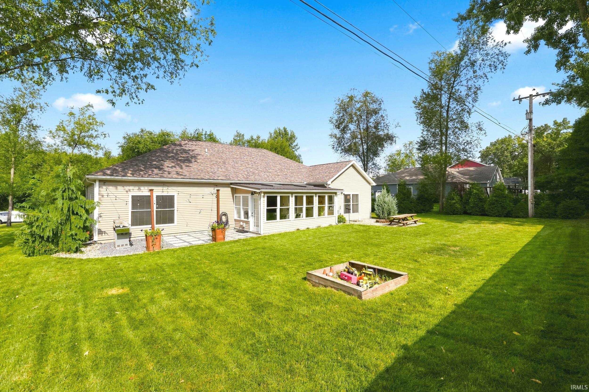 Expansive backyard featuring a lush lawn, mature trees, and a sunroom with multiple windows