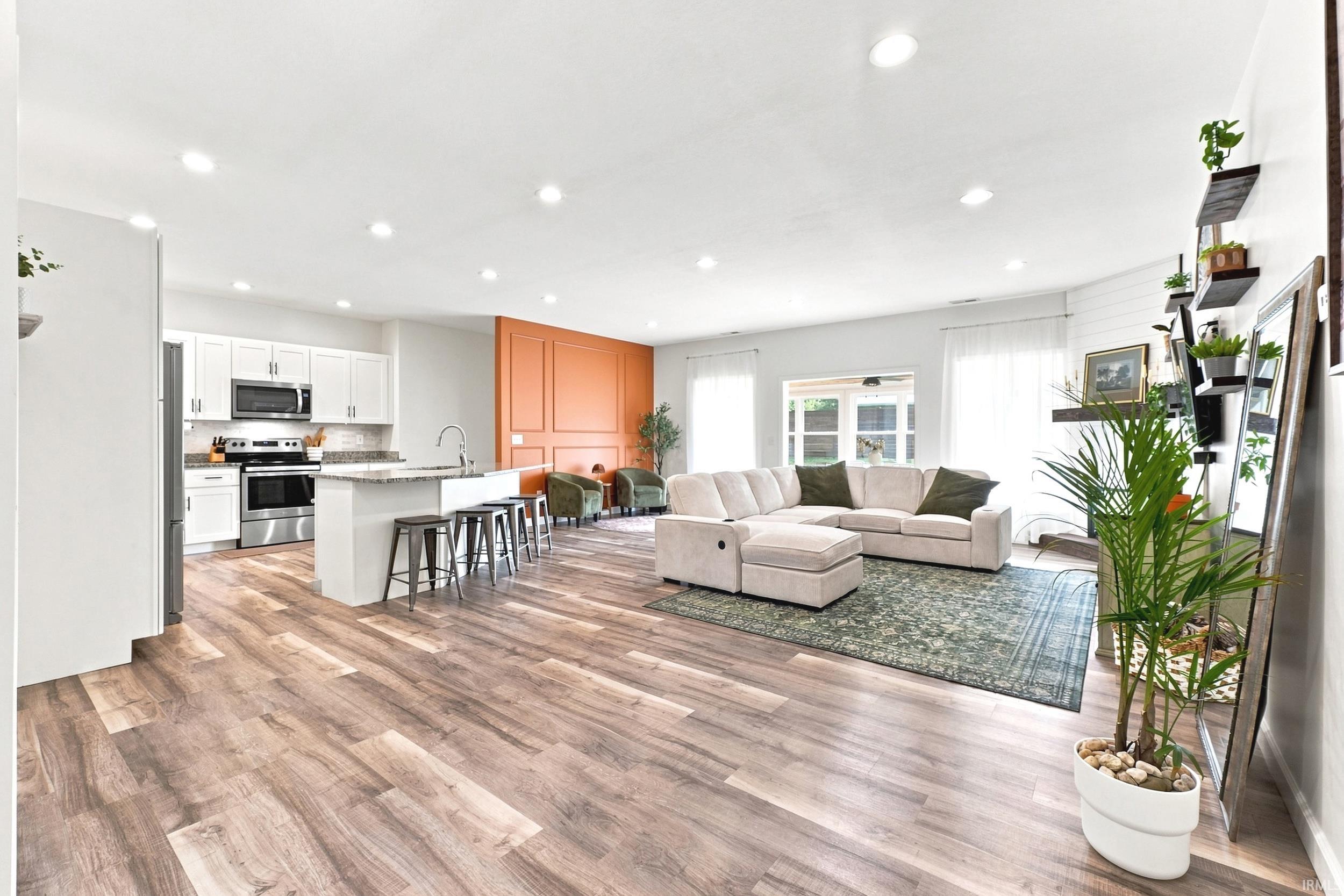 Open-concept living area featuring wood-finish flooring, recessed lighting, and a kitchen with white cabinetry and stainless steel appliances
