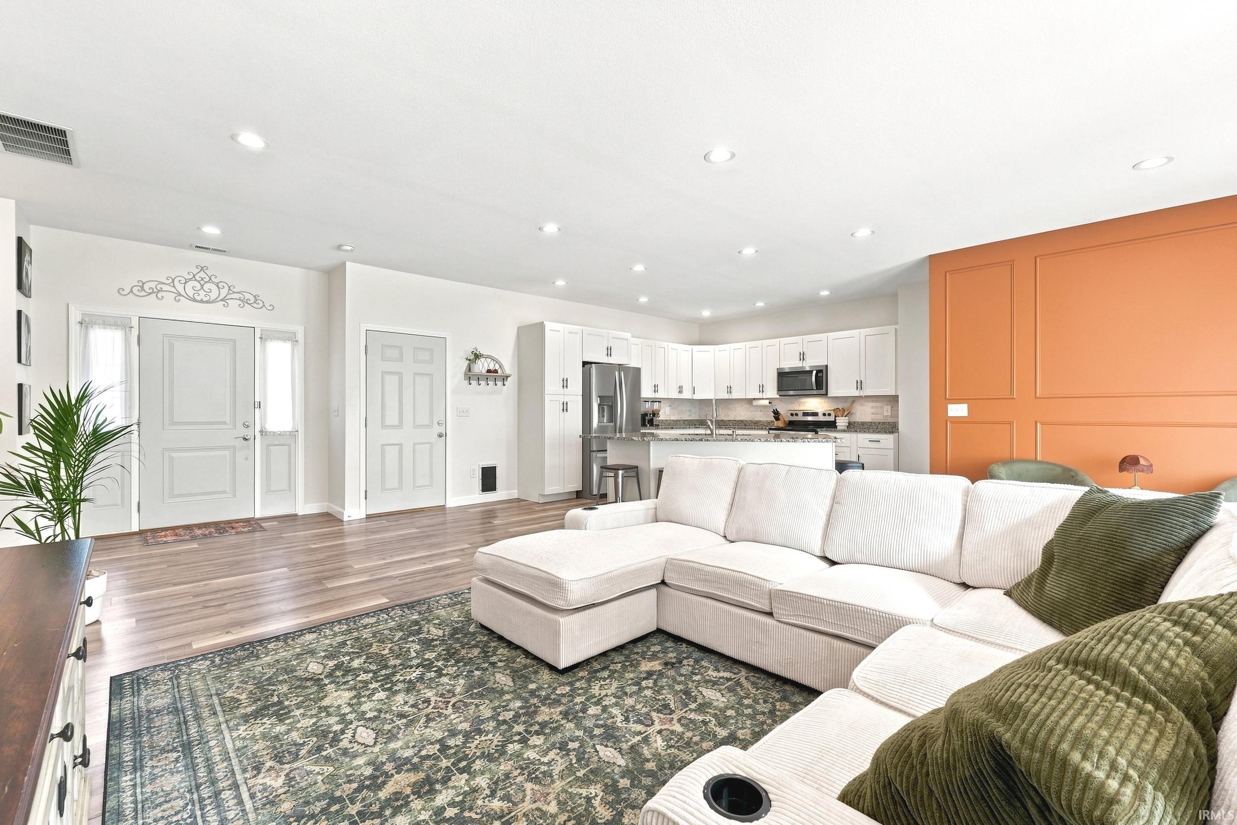 Open-concept living space with wood-finish flooring, recessed lighting, and a kitchen featuring white cabinetry, stainless steel appliances, and a breakfast bar