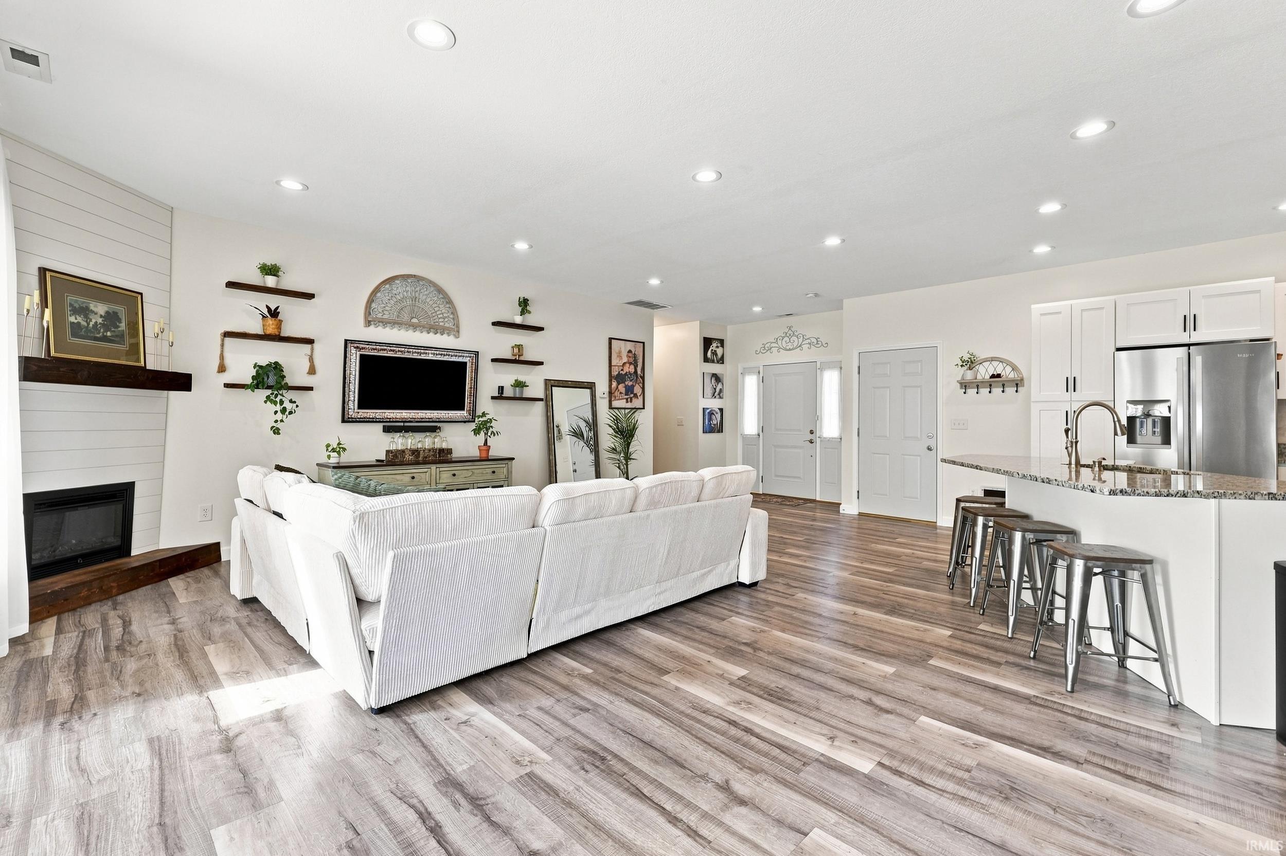 Open-concept living space featuring wood-finish flooring, recessed lighting, and a white shiplap-accented fireplace