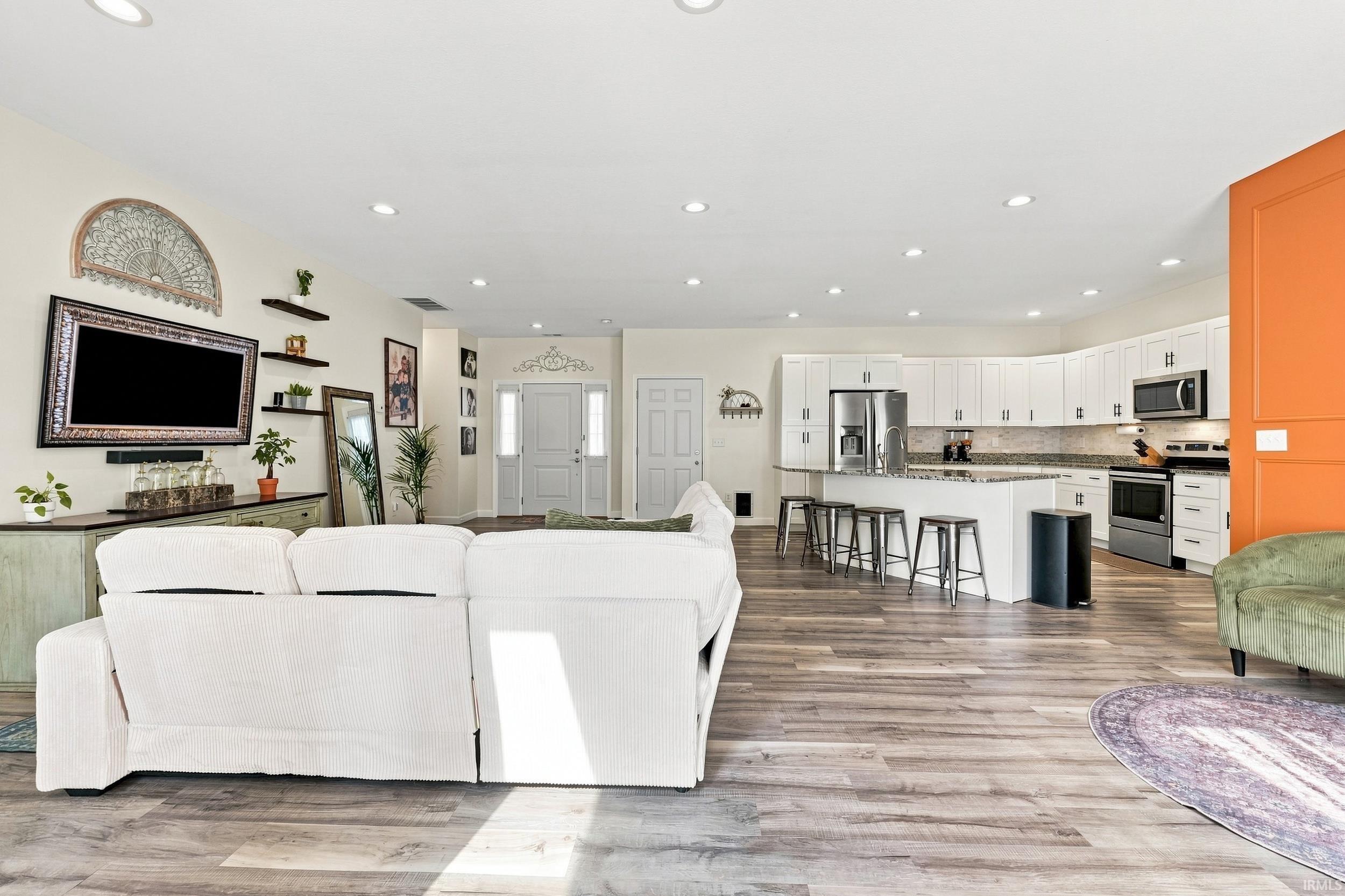 Open-concept living space featuring wood-finish flooring, recessed lighting, and a white kitchen with a peninsula island