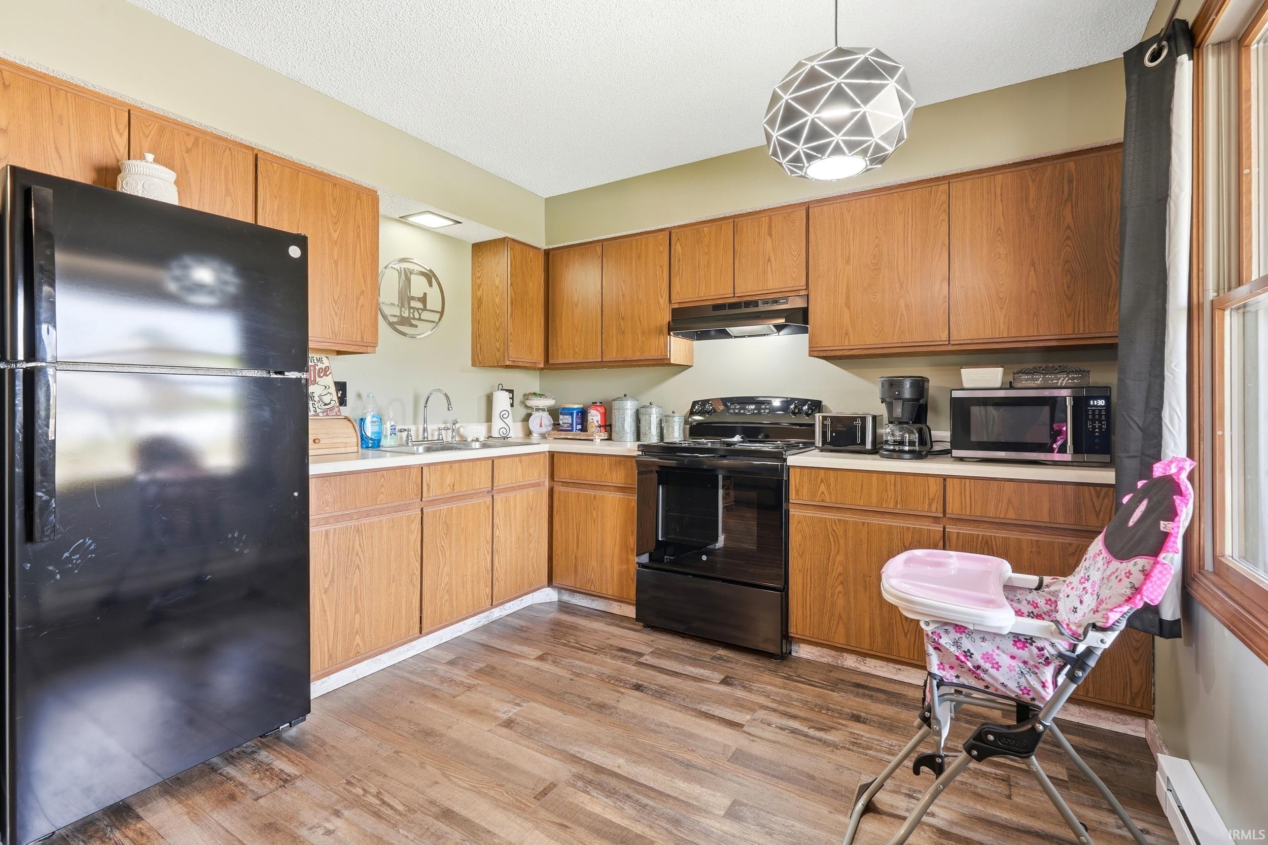 Kitchen featuring wood-finish flooring, ample cabinetry, L-shaped countertops, a stainless steel sink, and a geometric pendant light fixture