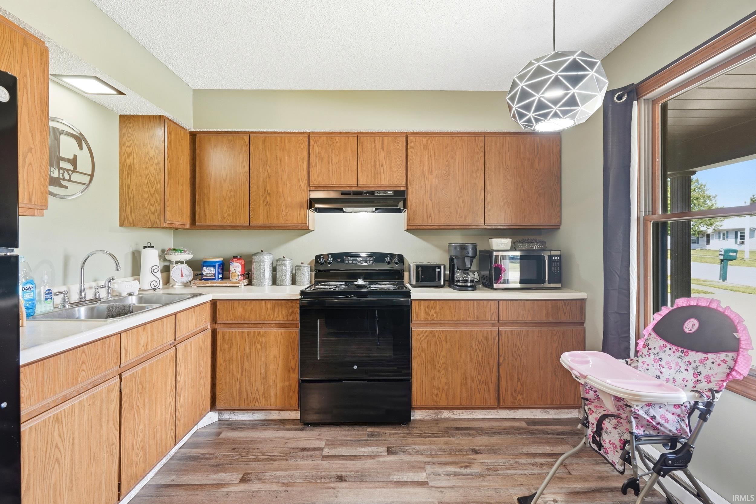 Kitchen featuring wood-finish cabinetry, light-toned countertops, a black range, and a double basin stainless steel sink