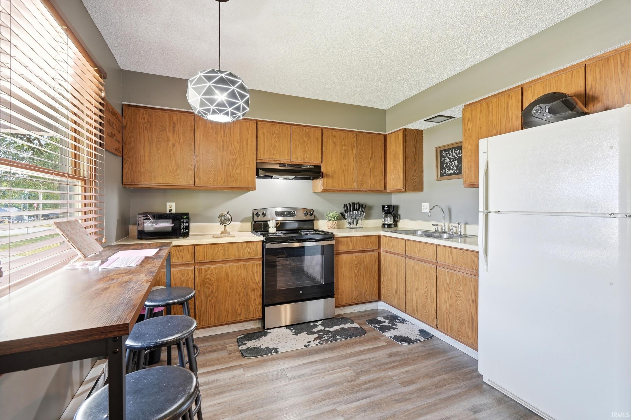 Kitchen featuring wood-finish cabinetry, stainless steel range and microwave, light-toned countertops, and wood-finish flooring