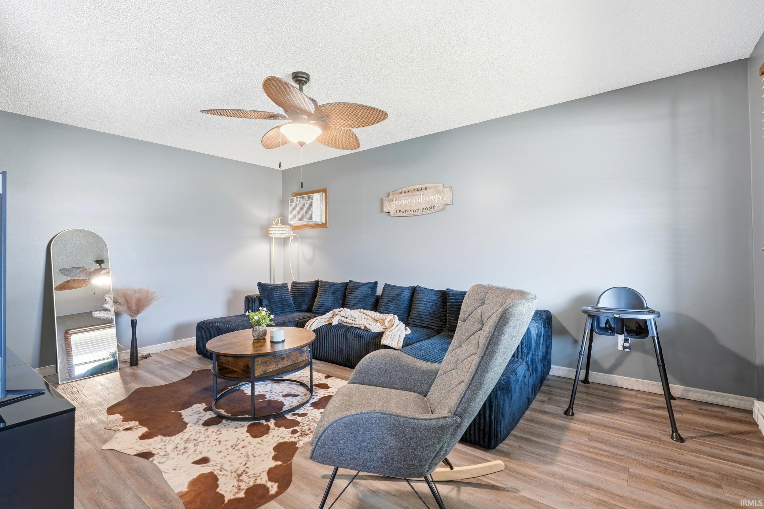 Living area featuring wood-finish flooring, light gray walls, and a ceiling fan with integrated lighting