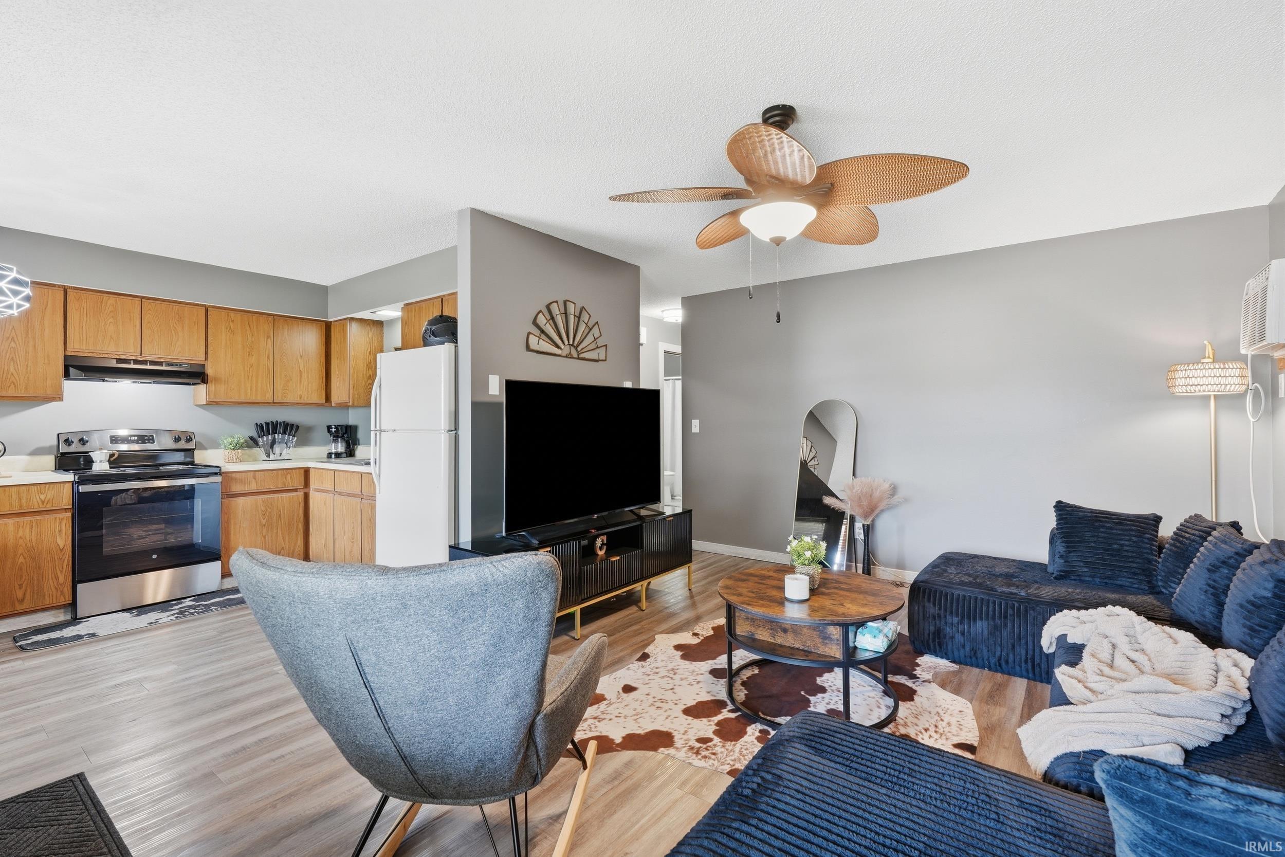Open-concept living area with wood-finish flooring, a ceiling fan with light fixture, and light gray walls