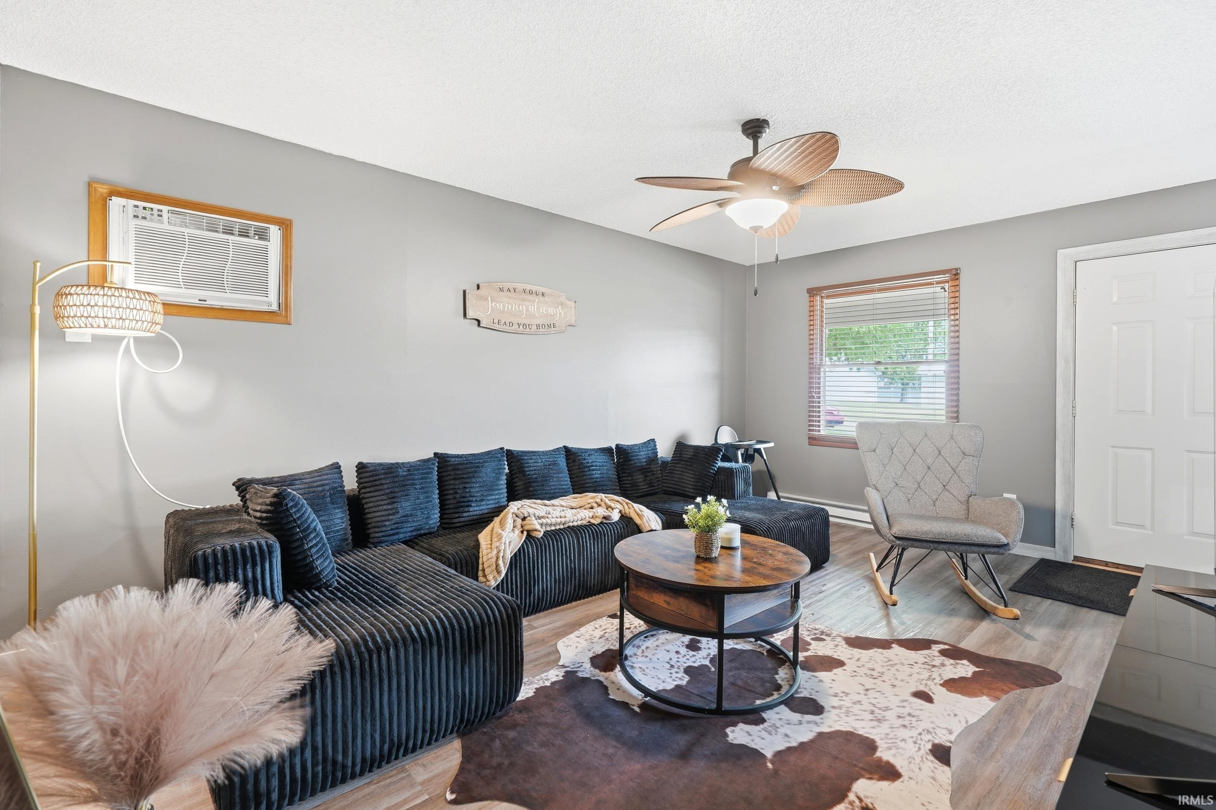 Living area featuring wood-finish flooring, a ceiling fan with integrated lighting, and a white paneled entry door